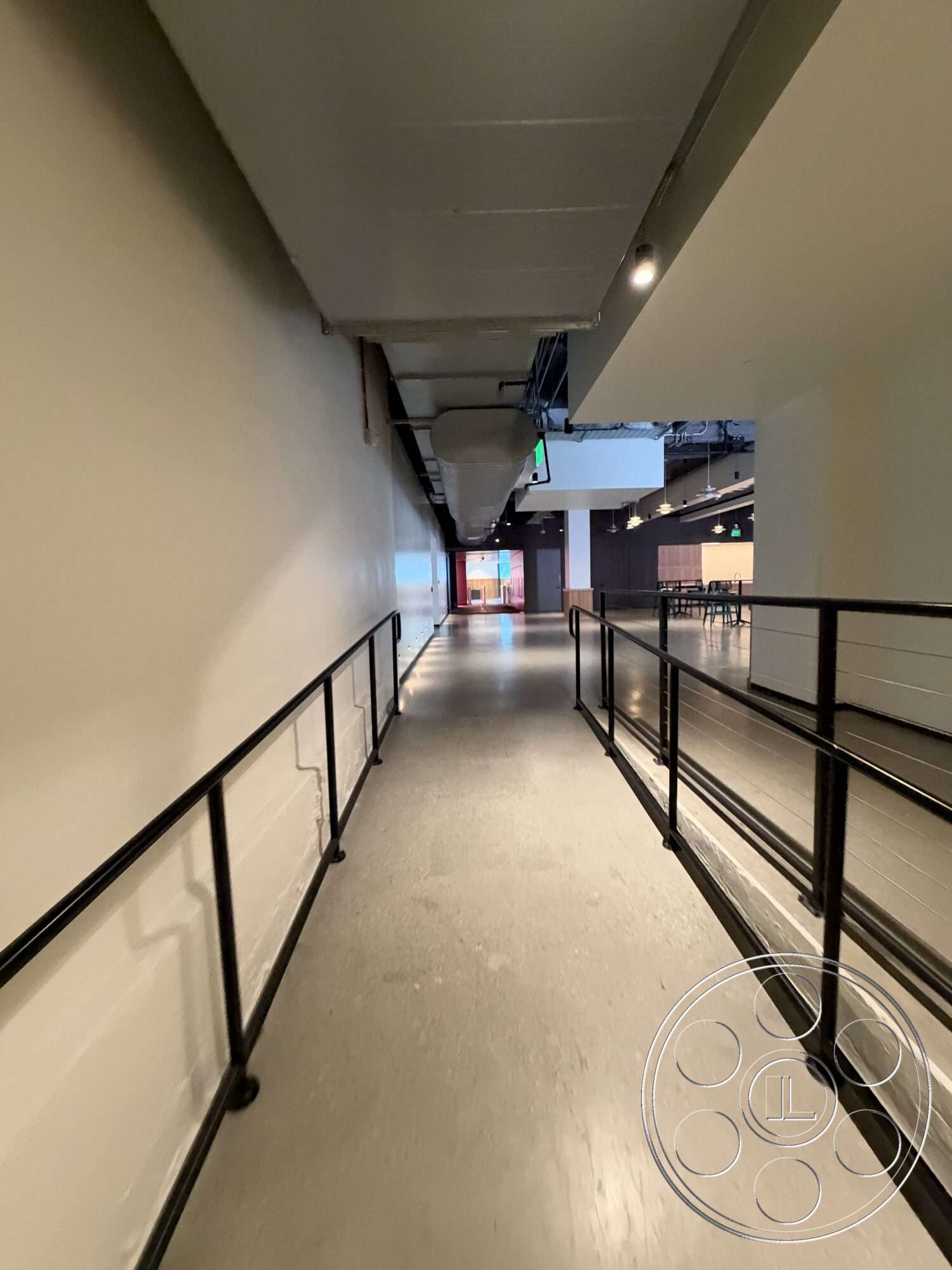 Office 130 - open layout, concrete flooring, metal railing, accessible pathway, modern industrial design, white painted walls, interior corridor, track lighting fixtures, exposed ceiling ducts