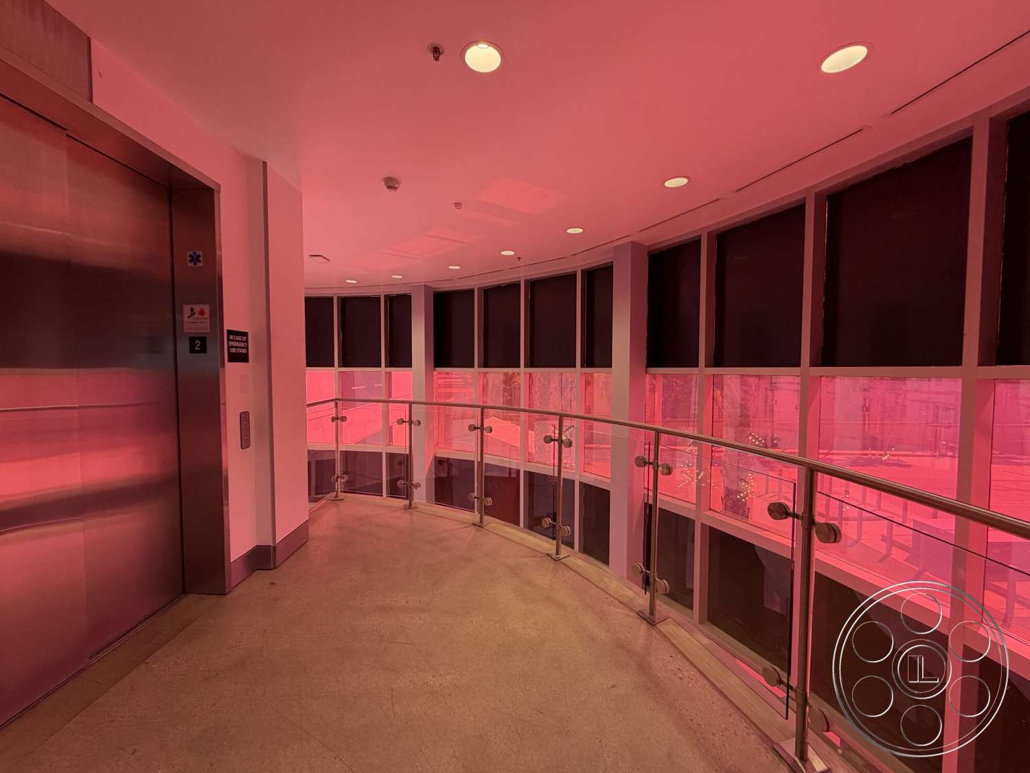 Office 130 - polished concrete floor, minimalist design elements, floor-to-ceiling windows, soft ambient lighting, interior hallway, modern architectural details, curved glass railing, metal elevator doors, round window shapes, interior signage