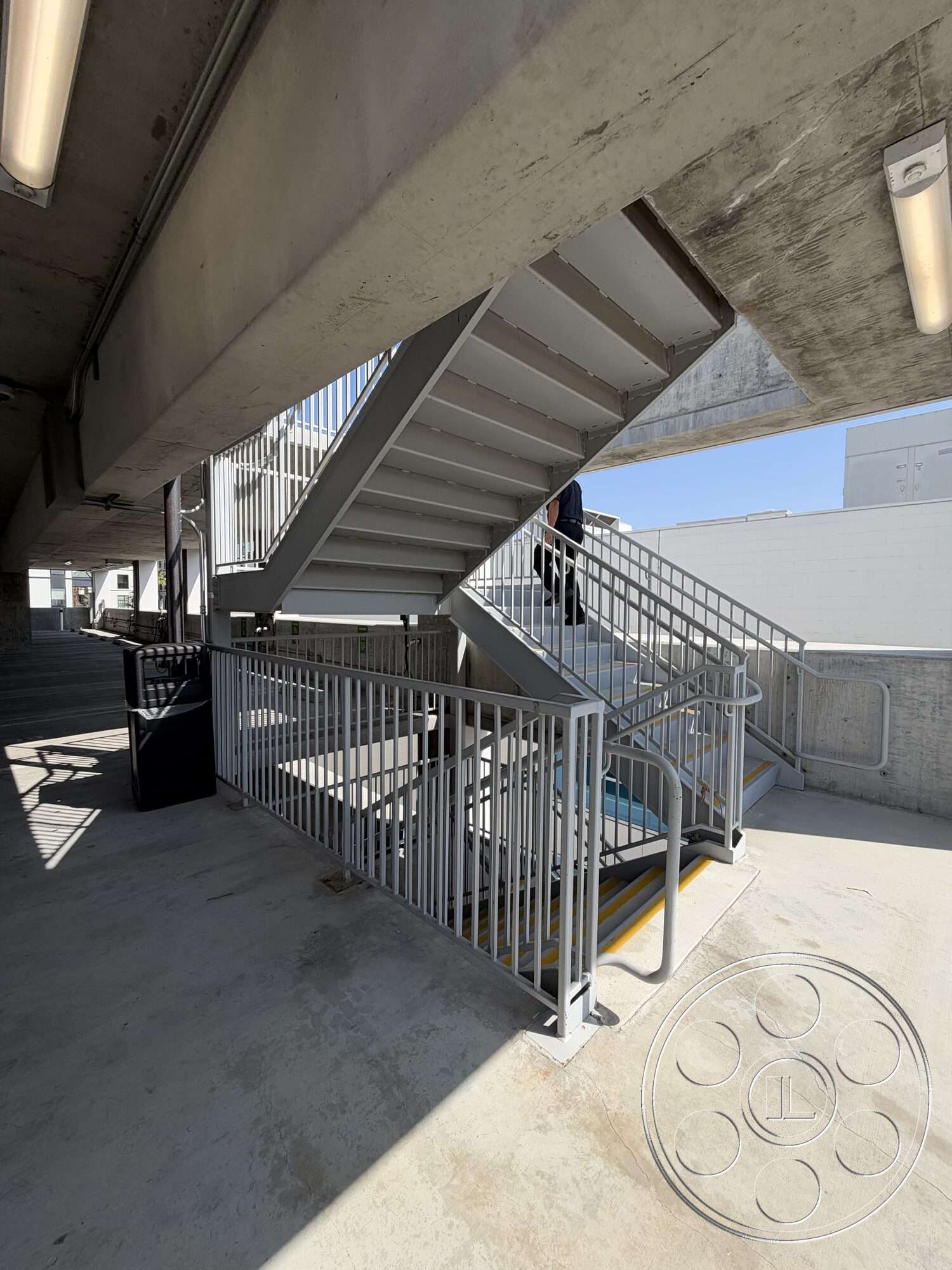 Office 130 - exposed concrete walls, metal handrail, steel staircase, industrial architectural style, interior concrete floor, open stairwell design, fluorescent ceiling lighting, concrete landing, public parking structure, metal grating near stairs