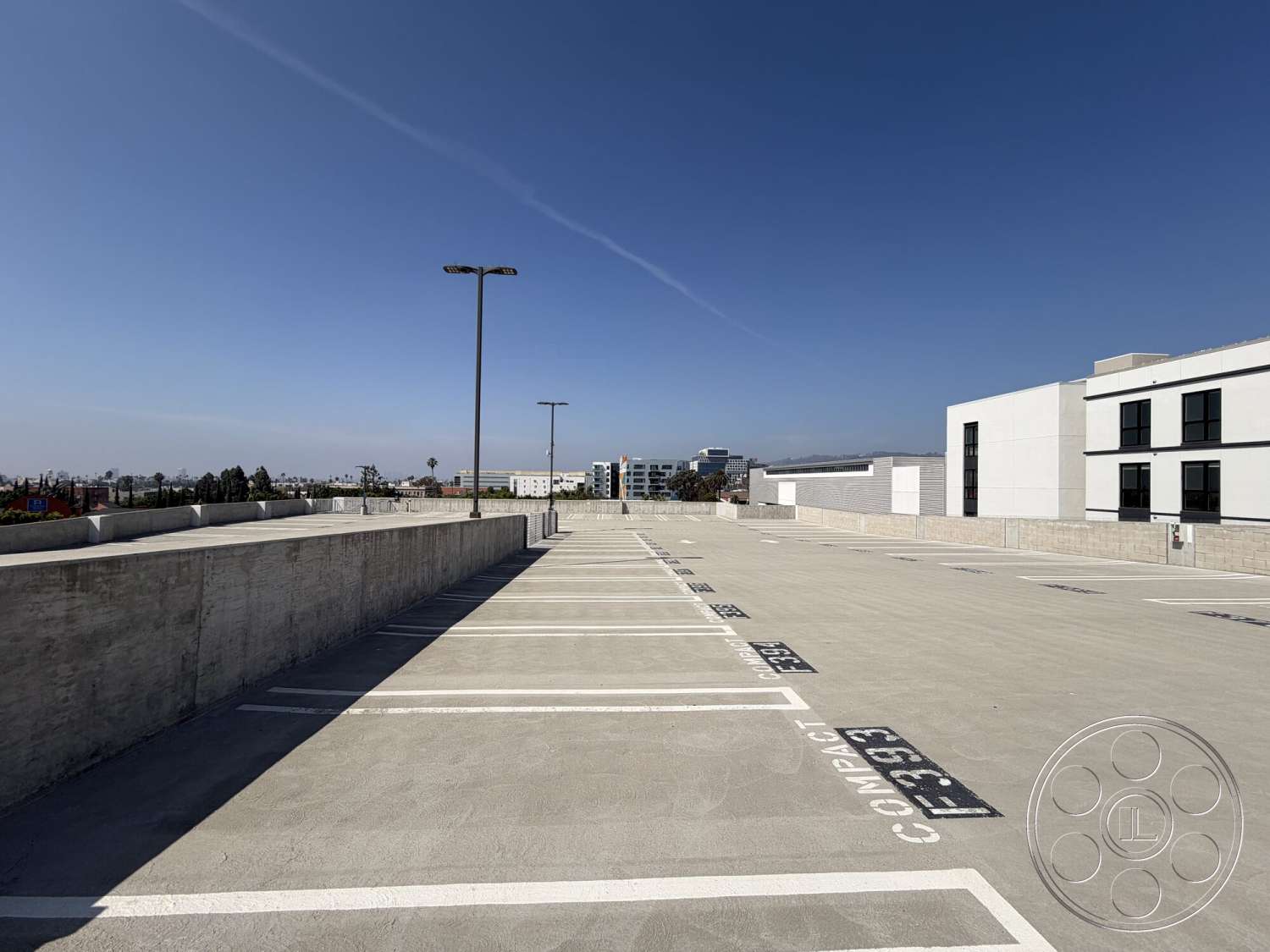 Office 130 - urban setting, flat roof design, open sky view, concrete parking lot surface, exterior wall cladding, commercial building environment, striped parking lines, modern building architecture, concrete barrier walls, exterior lighting poles, compact parking spaces