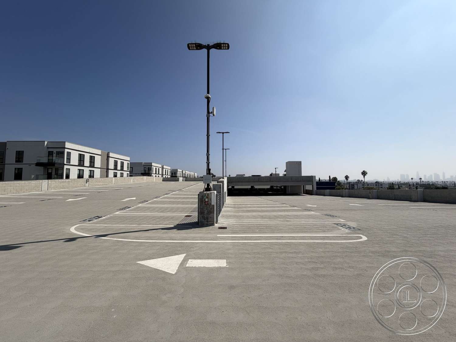Office 130 - exterior, urban skyline view, open-air setting, flat roof design, modern multi-story buildings, concrete parking lot surface, floor-mounted lighting fixtures, striped parking space markings, palm trees along perimeter