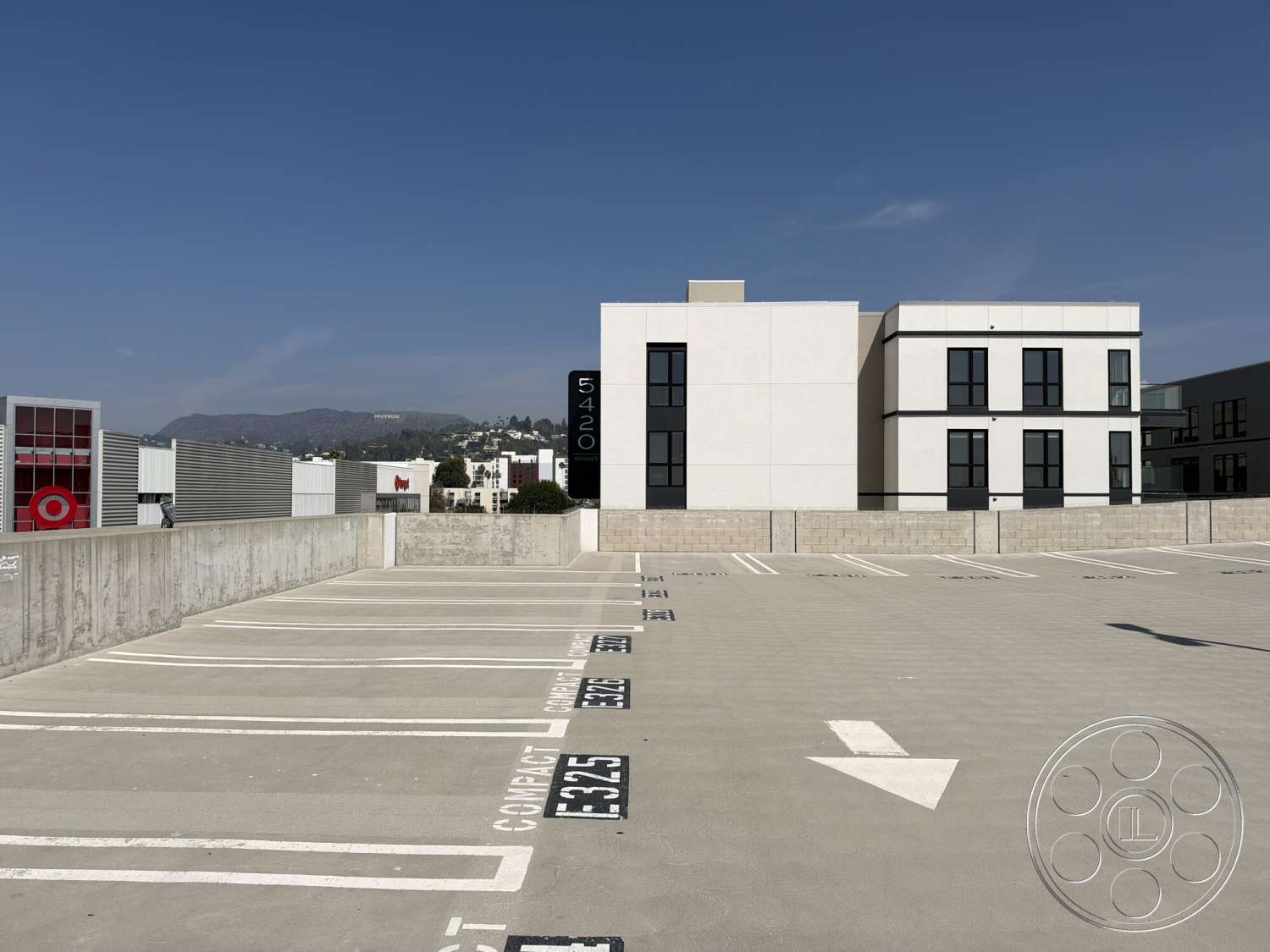 Office 130 - exterior, flat roof, modern architectural style, black window frames, large floor-to-ceiling windows, concrete parking lot, white stucco exterior walls, parking space markings, concrete wall border