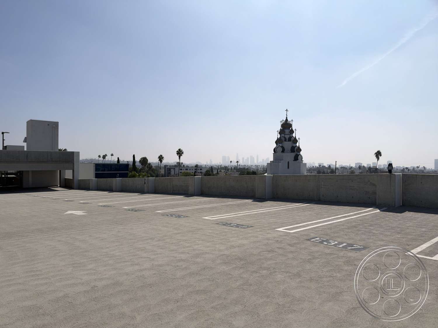 Office 130 - exterior, city skyline view, clear blue sky, surrounding palm trees, urban parking lot, concrete parking structure, flat concrete rooftop, decorative church dome