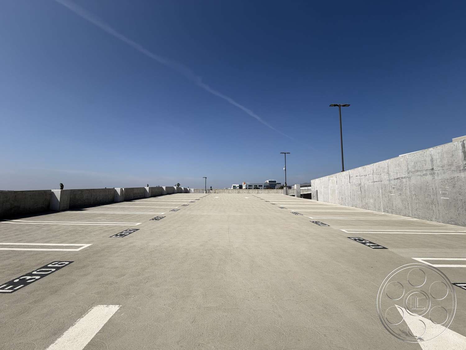 Office 130 - clear blue sky, concrete flat roof, concrete parking structure, open parking layout, striped parking lines, painted concrete parking surface, metal light poles, exterior skyline view