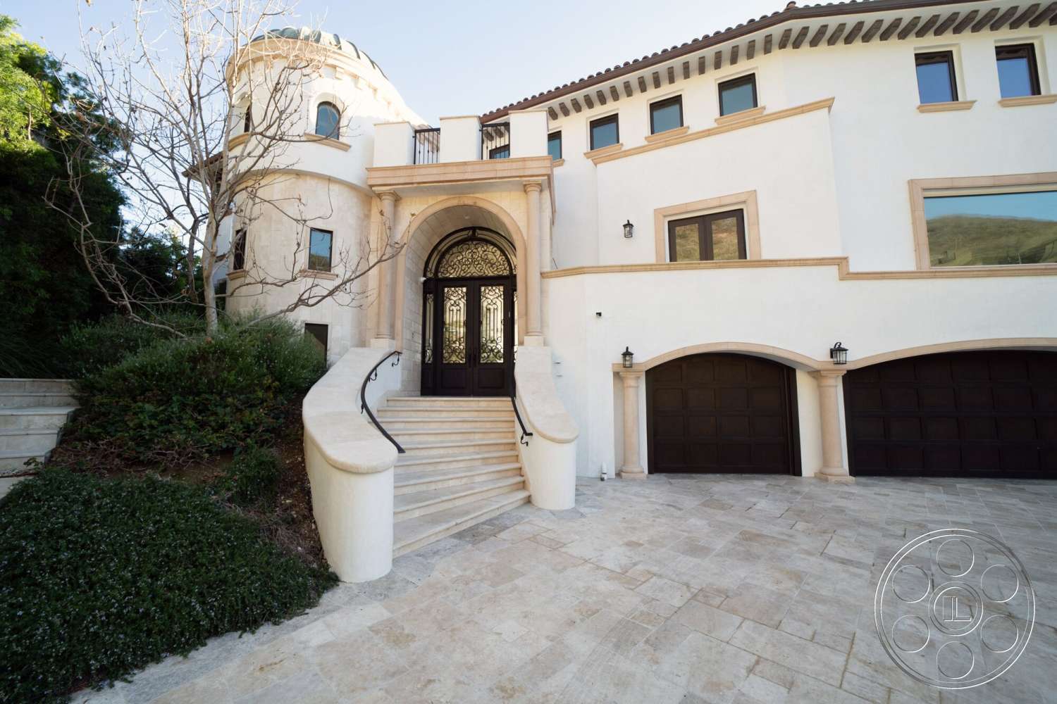 Medit 169 - exterior, landscaped garden, circular driveway, gabled roof, stucco walls, arched doorways, double front doors, metal light fixtures, symmetrical façade, stone staircase, balcony railing, marble entry steps, tile driveway, decorative window frames