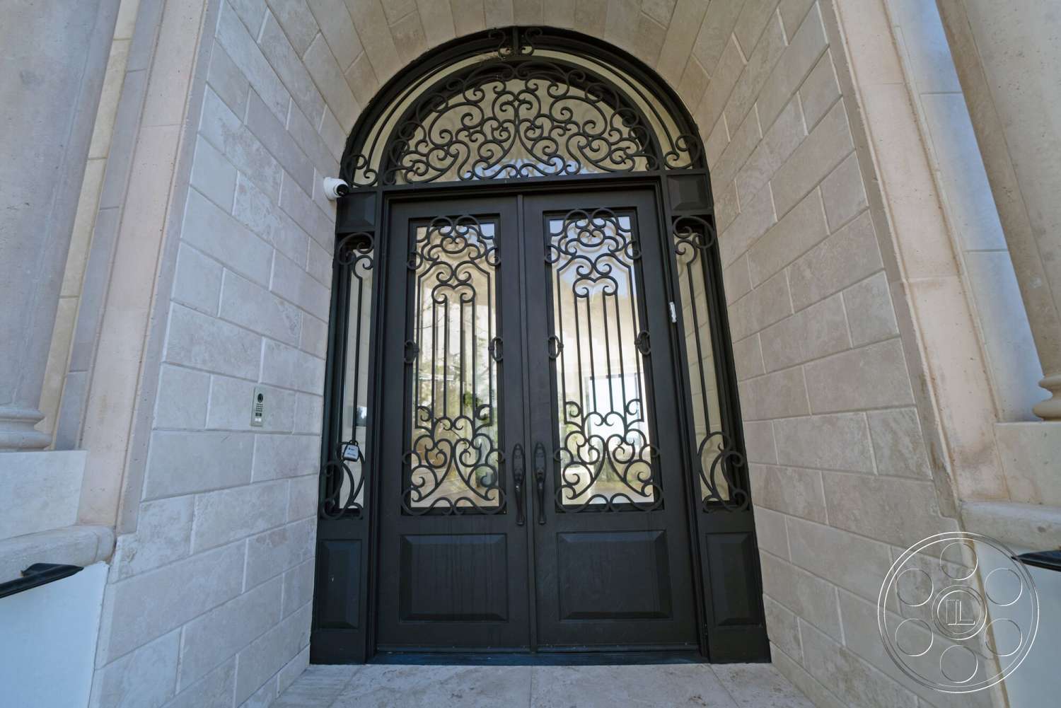 Medit 169 - arched door frame, transom window above door, double door entryway, limestone exterior walls, cast iron decorative door grille, smooth stone threshold, textured stone masonry, detailed wrought iron work