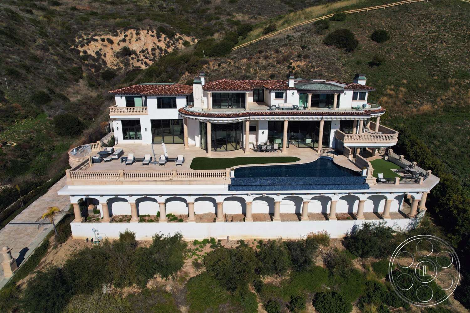 Medit 169 - exterior, large glass windows, outdoor living space, stucco walls, tile roof, Mediterranean architectural style, curved swimming pool, stone patio flooring, balcony with iron railings, landscaped hillside setting, rectangular pool deck, vaulted ceilings, arched colonnades, terrace seating area