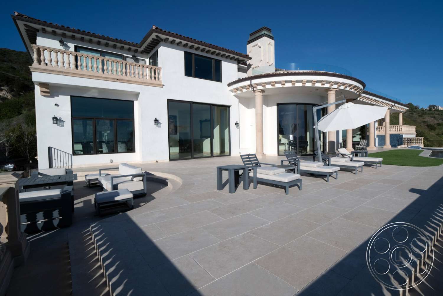 Medit 169 - exterior, white stucco walls, large glass windows, landscaped lawn, hillside location, Mediterranean architectural style, ceramic outdoor furniture, slate patio flooring, curved porch ceiling, stone balustrade, vaulted porch ceiling, pergola with umbrella, spacious outdoor seating area