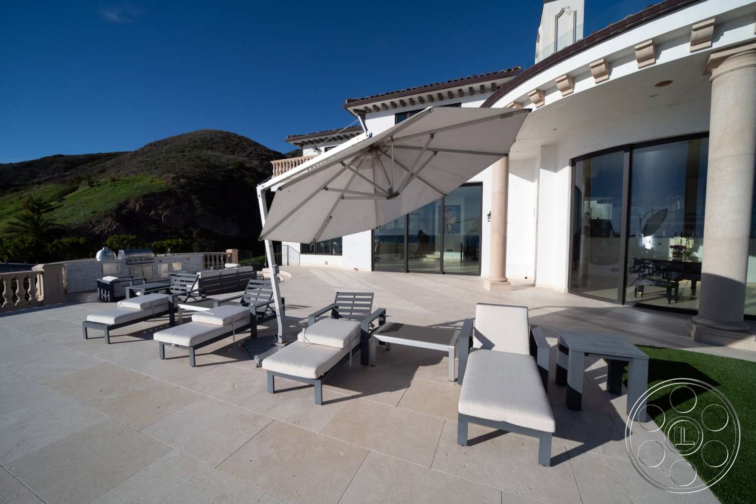 Medit 169 - exterior, glass sliding doors, modern outdoor furniture, outdoor dining area, mountain view, terracotta roof tiles, sunshade umbrella, concrete pool deck, stone columns, landscaped garden area, flagstone patio flooring, beach house setting