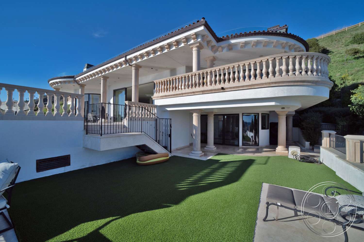 Medit 169 - exterior, flat roof, modern architectural style, stucco walls, outdoor living area, concrete patio flooring, city view setting, exposed stone columns, turf lawn, rounded balcony with decorative railing