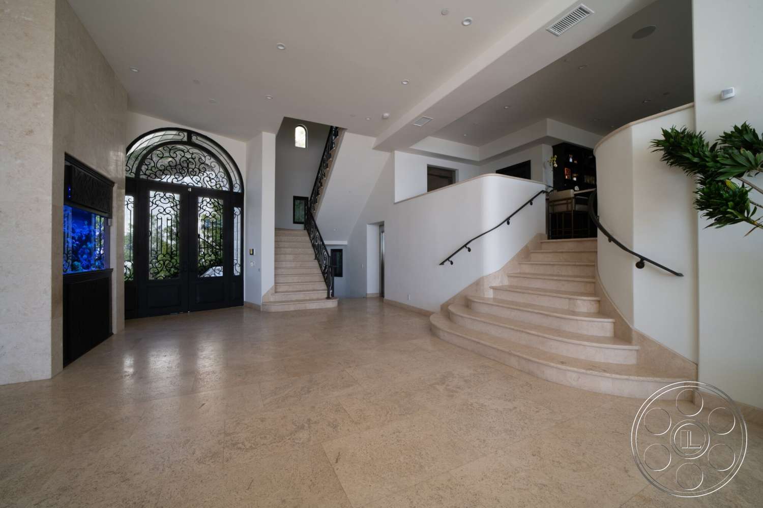 Medit 169 - large windows, recessed lighting, open floor plan, modern fixtures, stone flooring, vaulted ceiling, cream-colored walls, spacious entryway, curved staircase, wrought iron railing, double front doors with arched top, wall-mounted aquarium