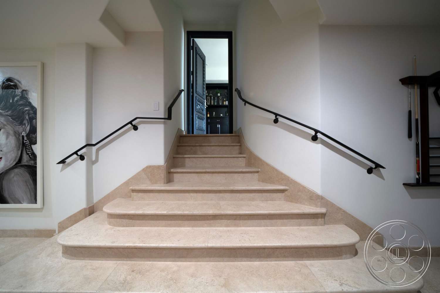 Medit 169 - modern aesthetic, open doorway, light-colored stone flooring, white painted walls, framed artwork on wall, curved staircase design, black metal handrail, beige limestone staircase