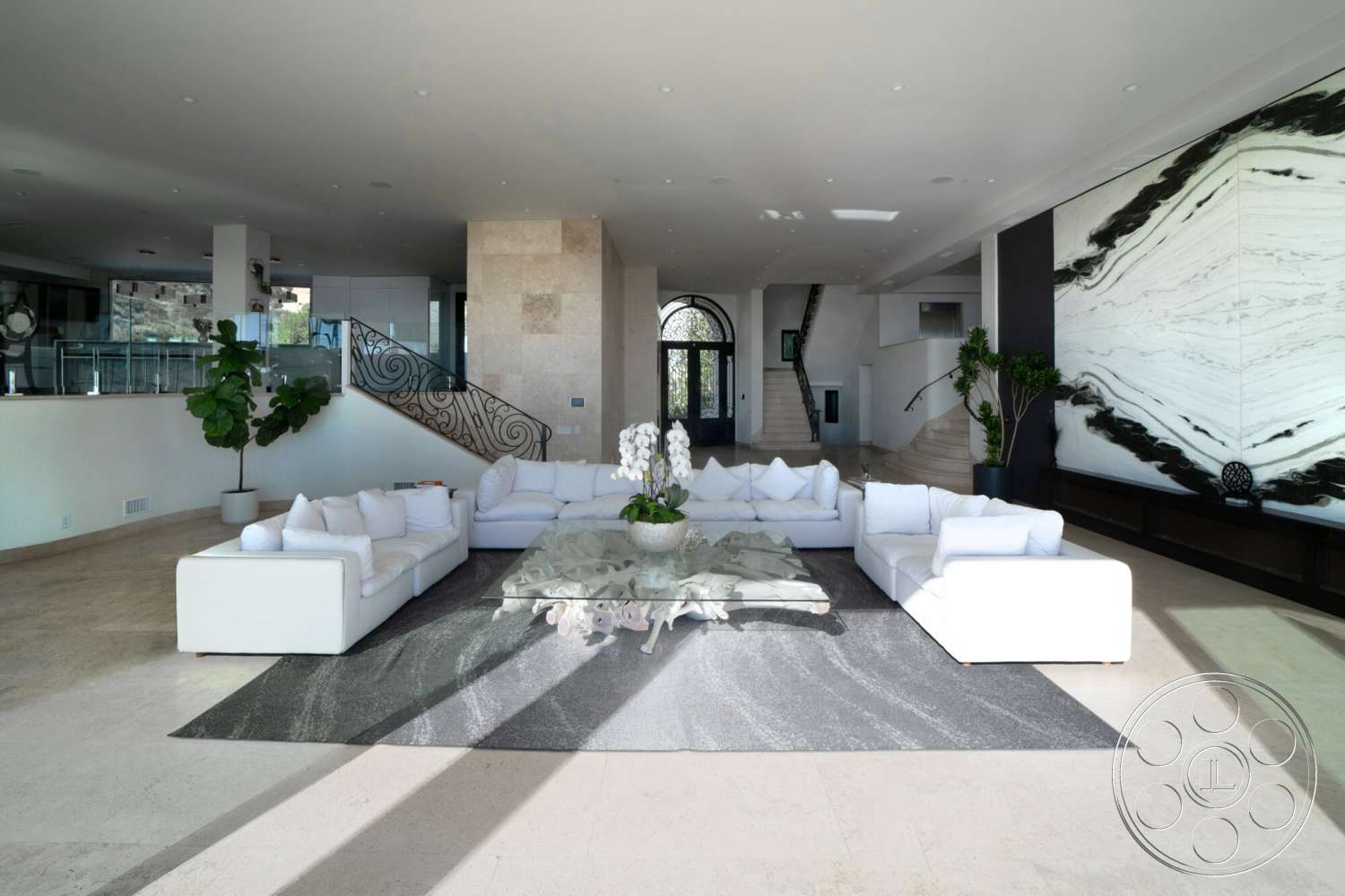 Medit 169 - textured area rug, glass coffee table, large glass windows, high ceiling, natural stone flooring, large potted plants, curved staircase, open-concept living area, modern sectional sofa, decorative indoor plants, metal stair railings, dark wood console table, cream marble tile flooring, expansive wall art
