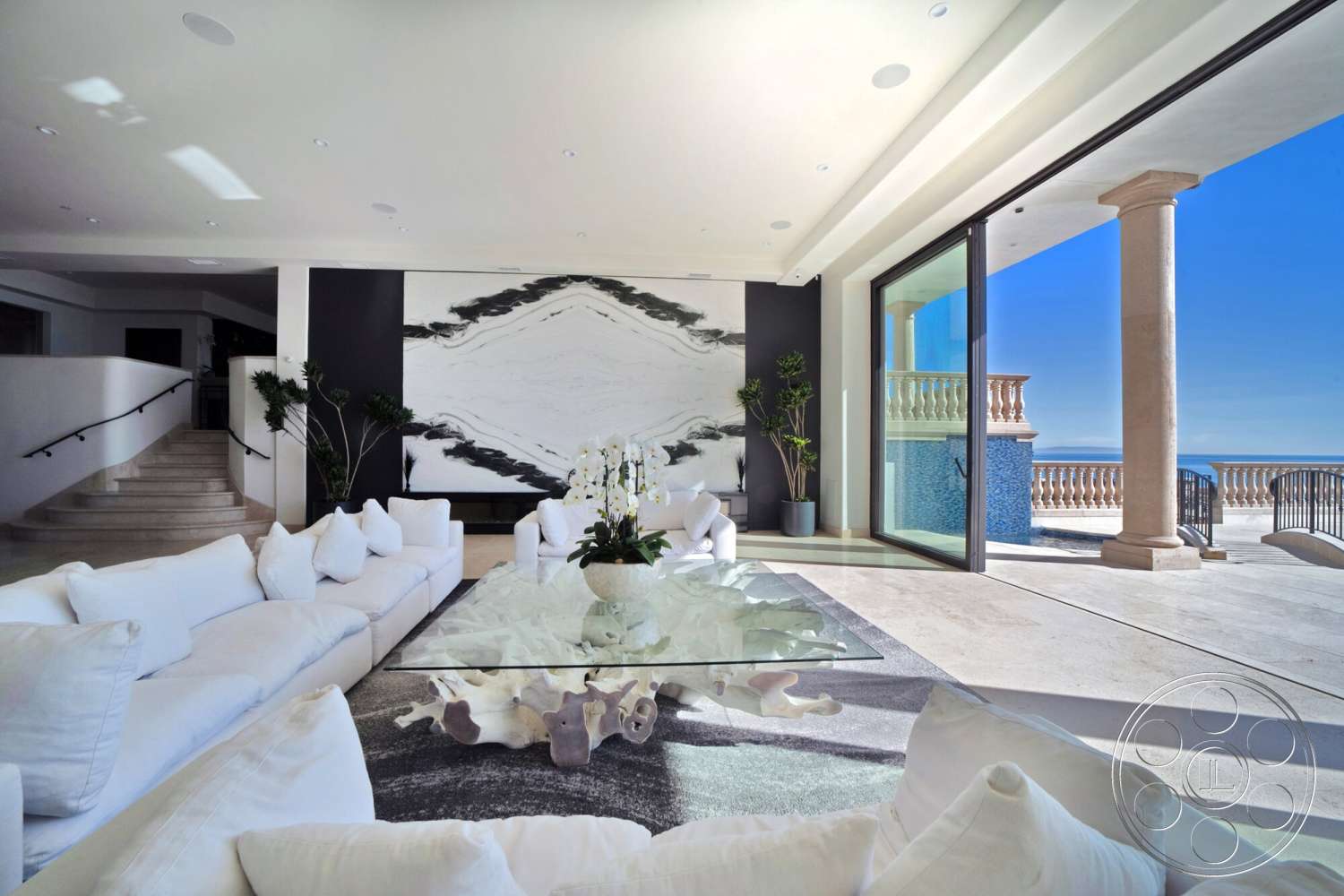 Medit 169 - minimalist decor, neutral color palette, natural light, contemporary design, indoor plants, textured area rug, open floor plan, smooth stone flooring, luxury living room, columned entry, modern ceiling lights, expansive glass sliding doors, white fabric sofa with cushions, glass coffee table with organic shape base, black and white marble accent wall