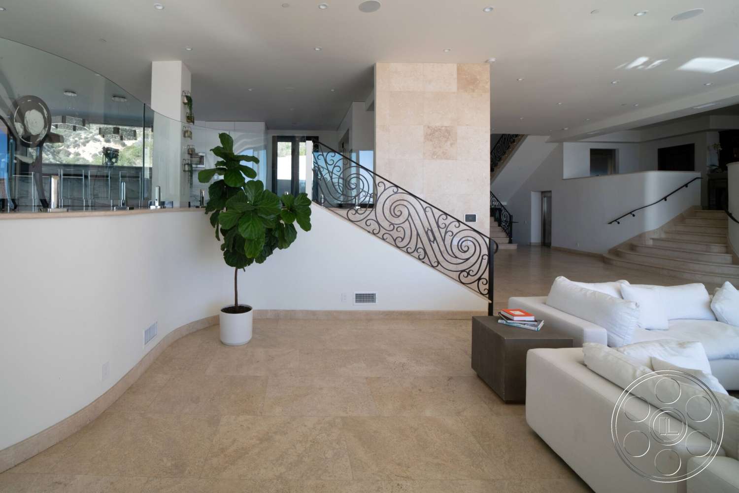 Medit 169 - open floor plan, floor-to-ceiling windows, recessed ceiling lighting, living room seating area, modern minimalist sofa, black wrought iron staircase railing, curved glass wall, travertine flooring, light-colored stone wall feature, tall indoor plant in a white pot