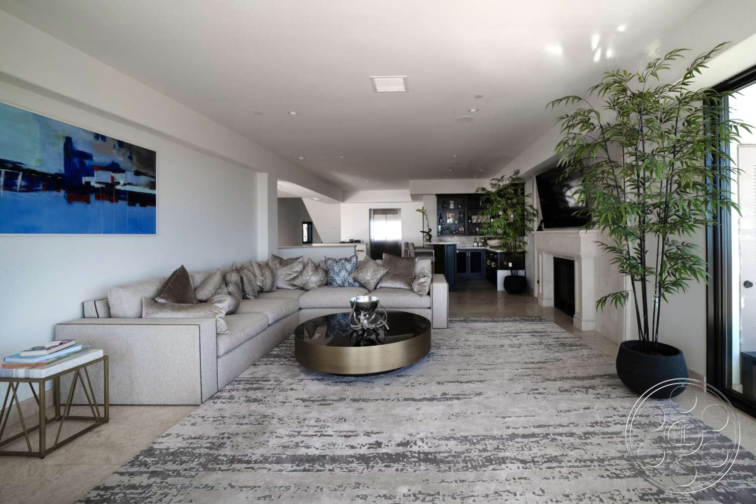 Medit 169 - natural light, modern decor, round coffee table, light-colored walls, sectional sofa, open concept layout, floor-to-ceiling windows, abstract artwork, built-in cabinetry, metal side table, accent pillows, fireplace with stone surround, tall indoor plants, tan stone flooring