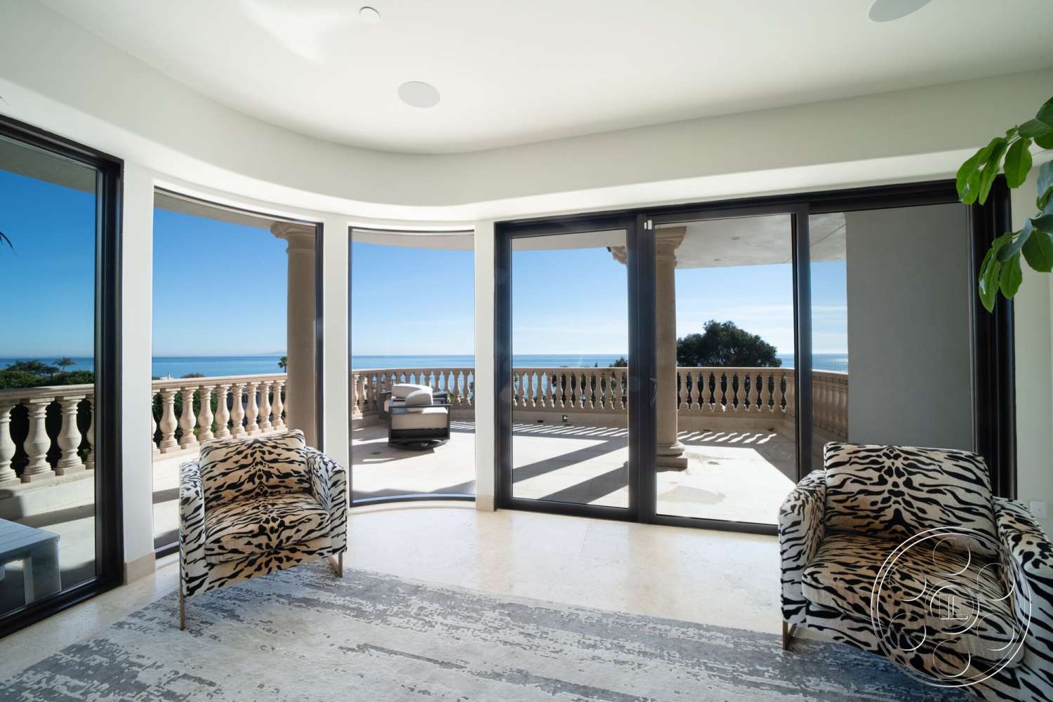 Medit 169 - spacious living area, natural stone flooring, white plaster walls, floor-to-ceiling glass doors, sunlit room, ocean view setting, curved window walls, beige marble floor tiles, modern balustrade design, tiger print accent chairs
