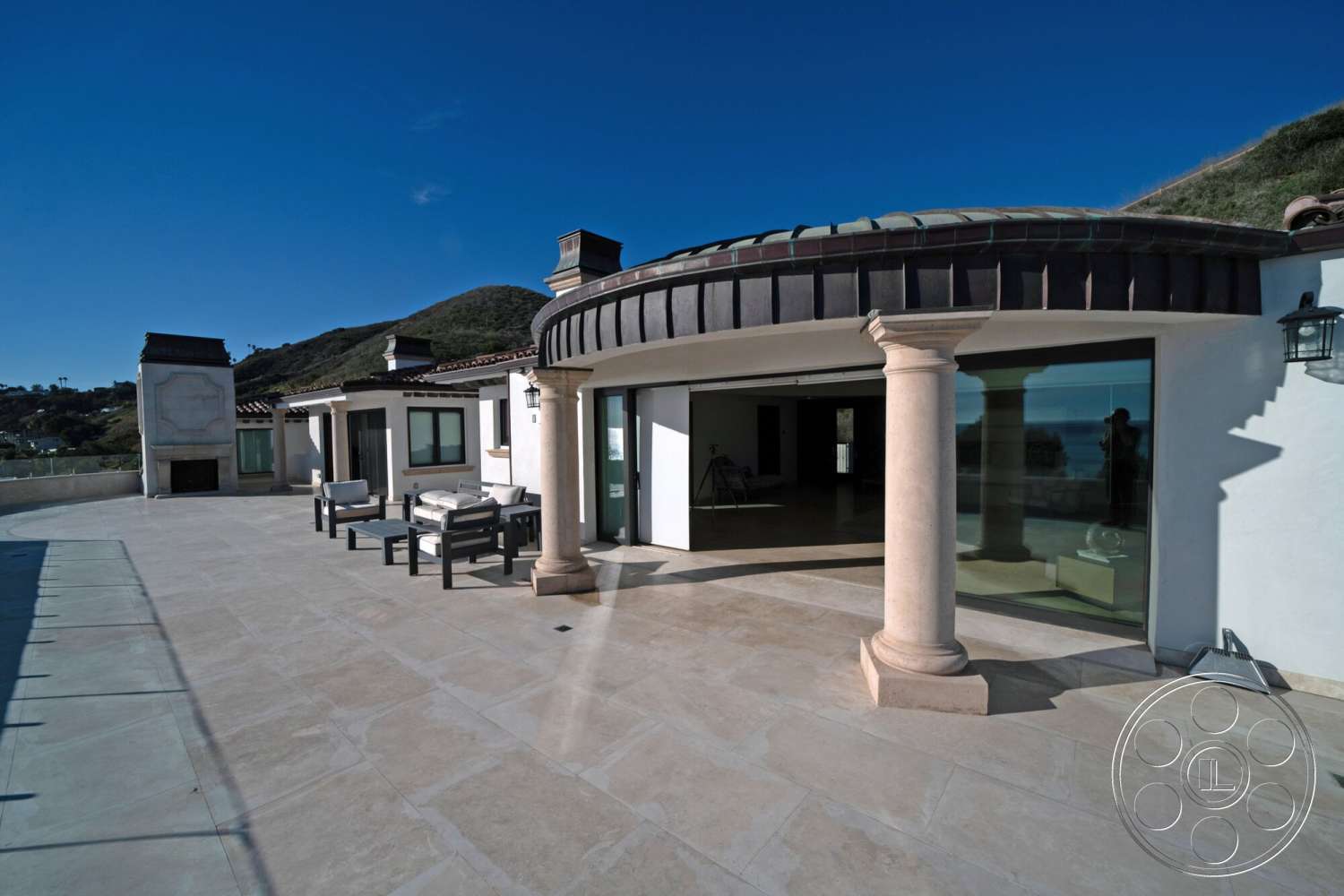 Medit 169 - exterior, terracotta roof, mountain view setting, stone patio flooring, floor-to-ceiling glass doors, modern Mediterranean architectural style, plaster exterior walls, fireplace feature wall, curved outdoor terrace, round column supports