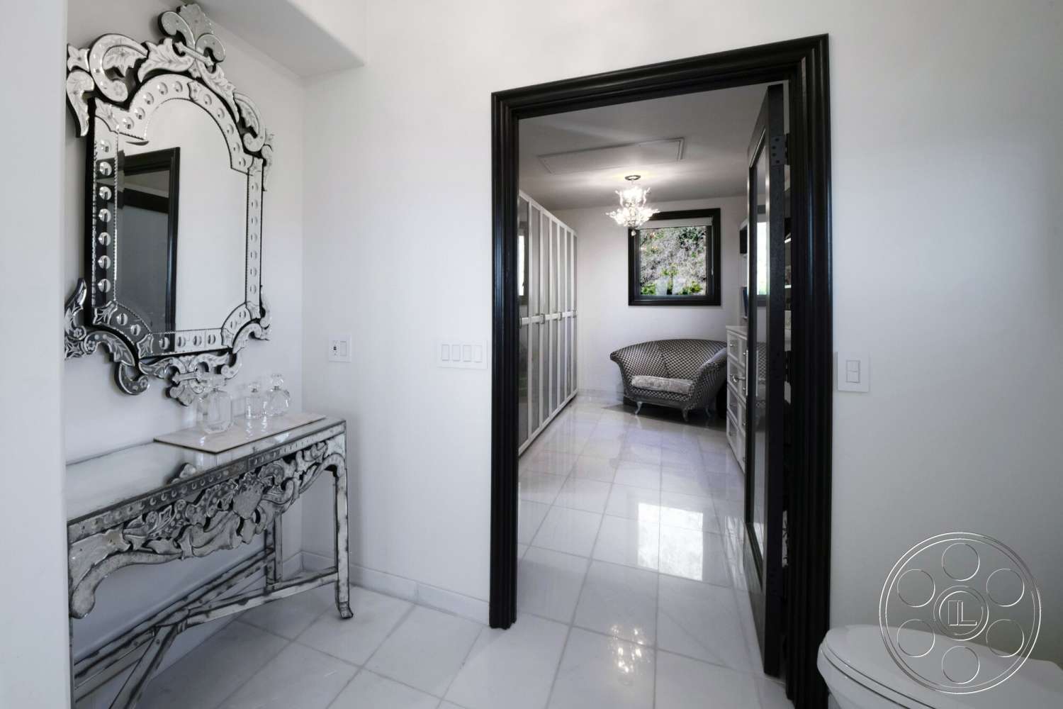 Medit 169 - neutral color palette, crystal chandelier, polished marble flooring, white painted walls, black-framed windows, decorative mirrored console table, ornate wall mirror, glass wardrobe doors, elegant lounge chair