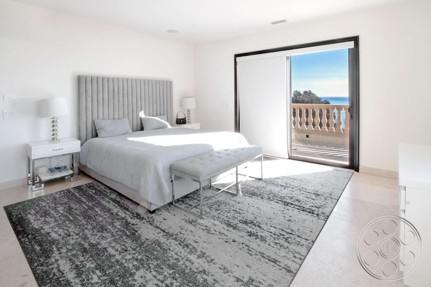 Medit 169 - gray upholstered headboard, polished marble flooring, plush area rug, white painted walls, floor-to-ceiling sliding glass doors, ocean view balcony, contemporary bedside lamps, soft beige bedding, silver bedside table, minimalist footstool