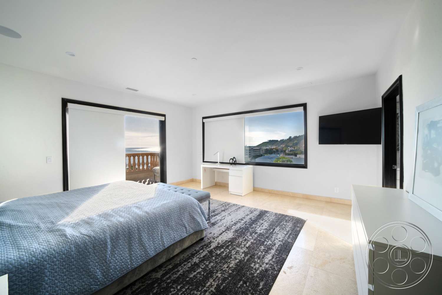 Medit 169 - black framed windows, textured plaster walls, beige stone flooring, neutral color scheme, minimalist bedroom design, wall-mounted flat screen TV, queen-sized bed with blue quilt, white modern desk, open view patio door