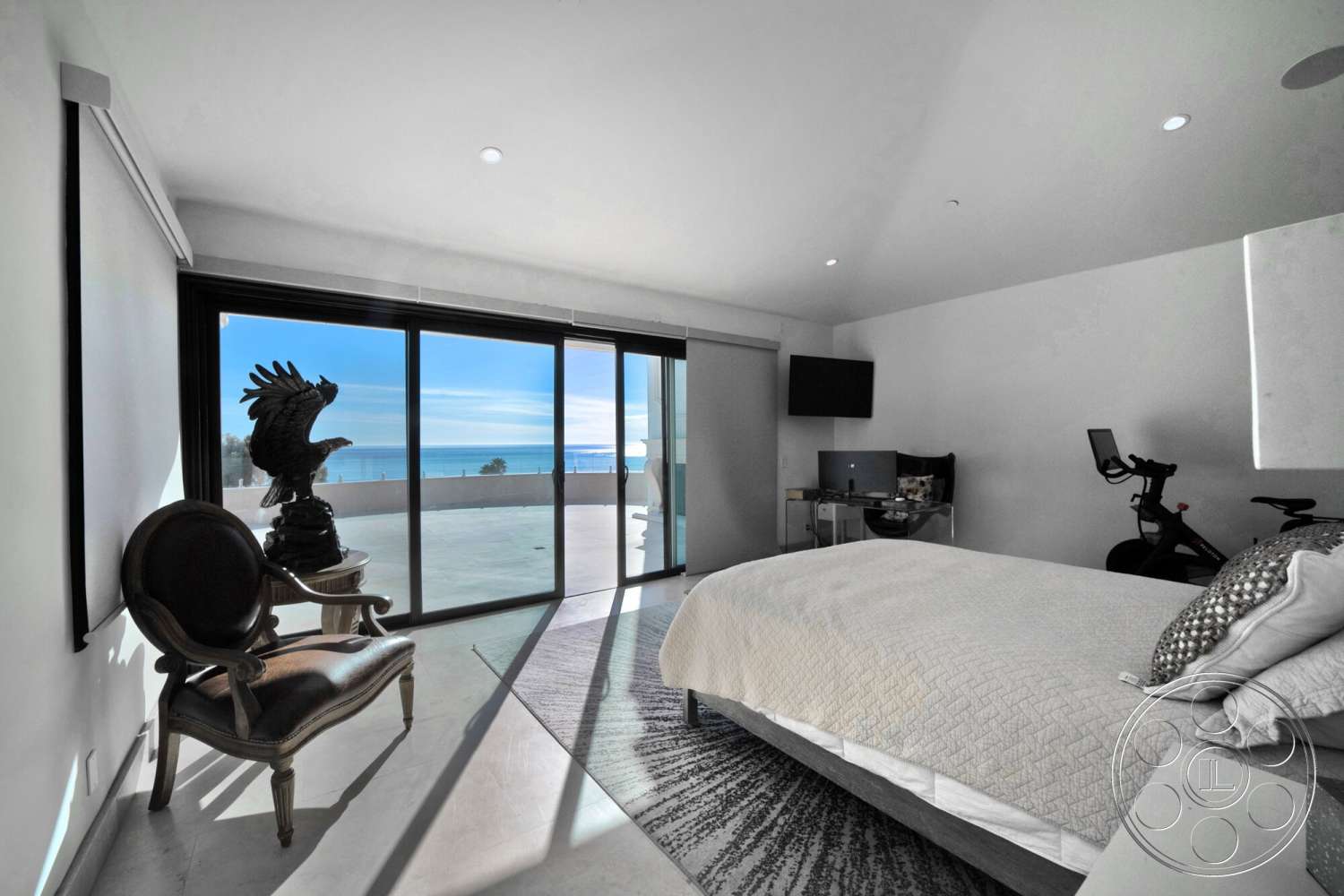 Medit 169 - minimalist design, contemporary decor, concrete flooring, large floor-to-ceiling windows, white painted walls, oceanfront view, modern accent chair, stylish desk area, queen-size bed with textured bedding, sitting area with coastal view, surface-mounted LED lighting, stylized statue artwork, exercise bike in corner
