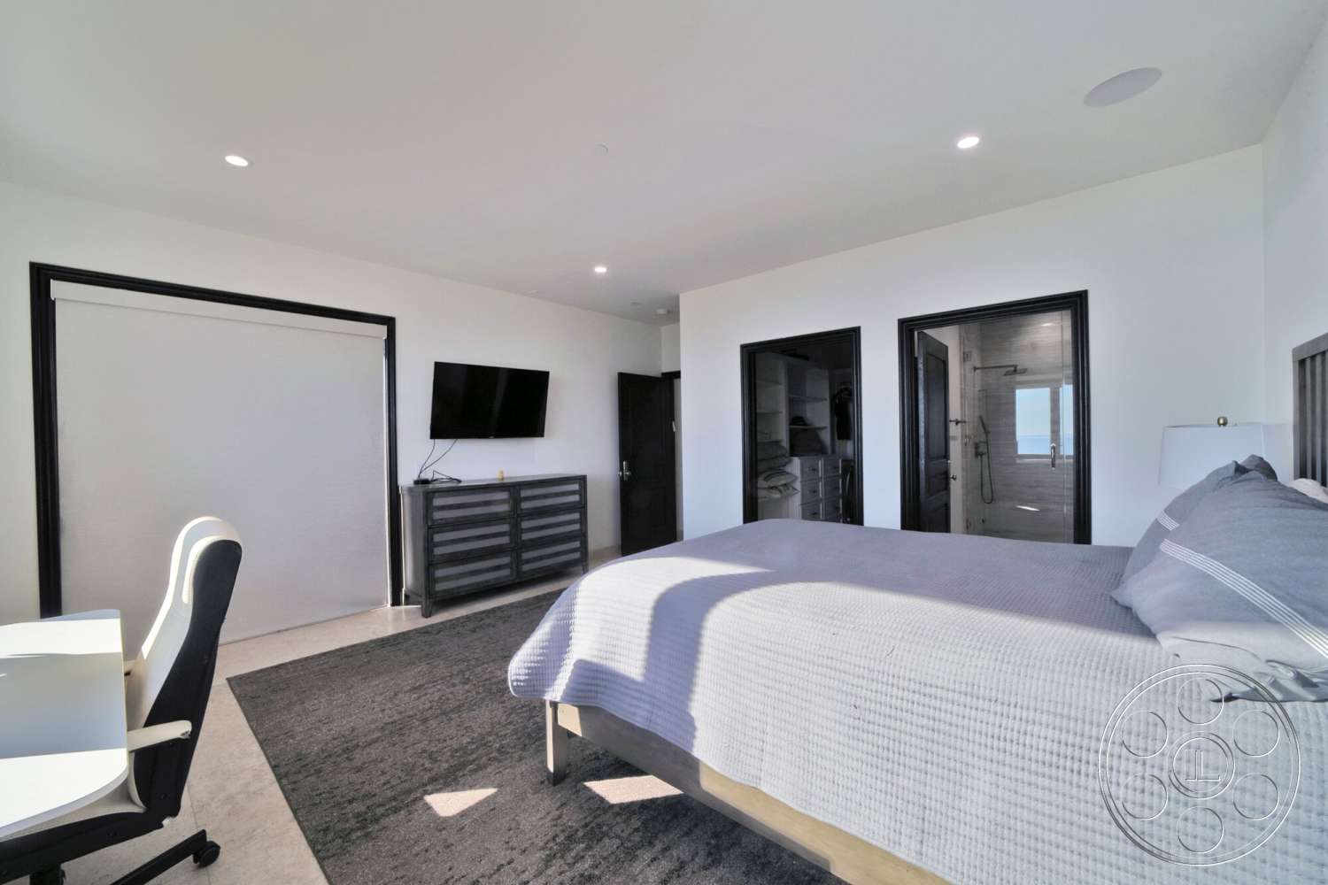 Medit 169 - recessed ceiling lights, hardwood bedroom floors, modern wooden dresser, white painted walls, large windows with ocean view, contemporary desk chair, textured gray area rug, black frame doors, king-size bed with light gray bedding