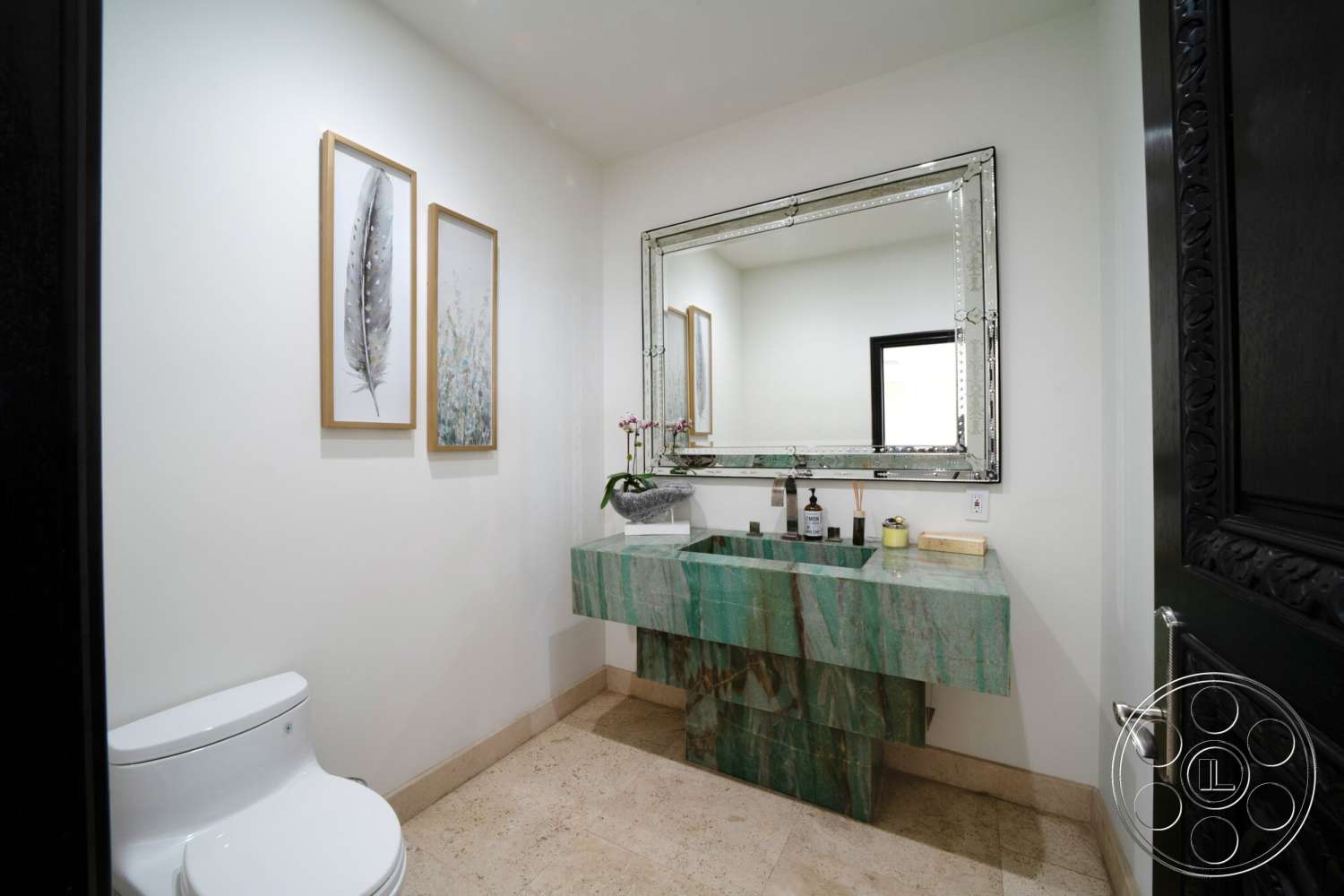 Medit 169 - framed wall art, mirror with decorative frame, white painted walls, modern toilet, marble bathroom countertop, green marble vanity, beige stone bathroom flooring, black wooden door with intricate design