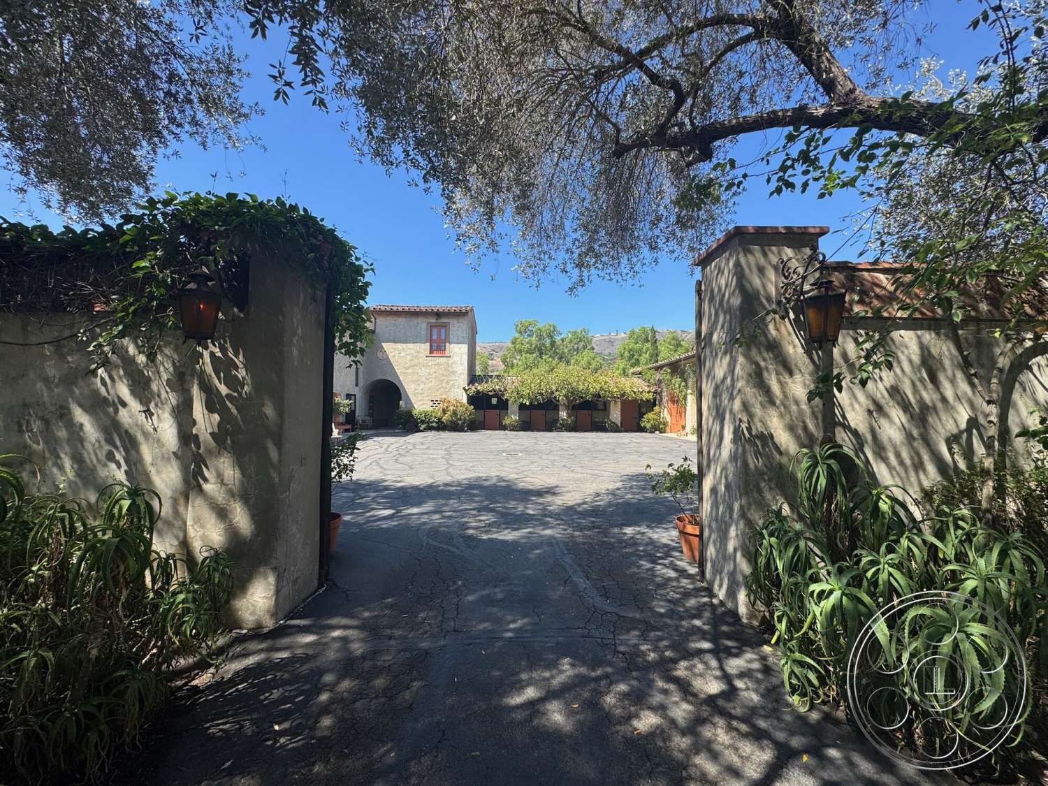 Farmstead Garden - exterior, landscaped garden, stucco walls, arched entryway, wood-framed windows, stone accent walls, courtyard setting, paved courtyard driveway, metal wall lanterns, olive tree setting