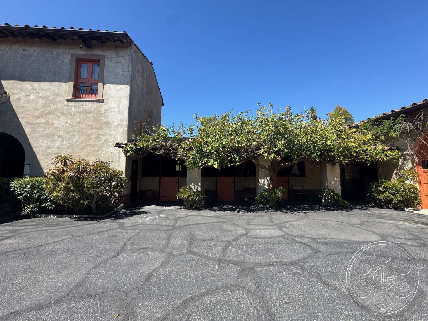 Farmstead Garden - exterior, paved driveway, exposed wooden beams, suburban setting, terracotta roof tiles, textured plaster walls, wooden window frames, Mediterranean architectural style, arched openings, landscaped garden beds, stucco wall finishes, vines covering pergola, decorative wooden doors