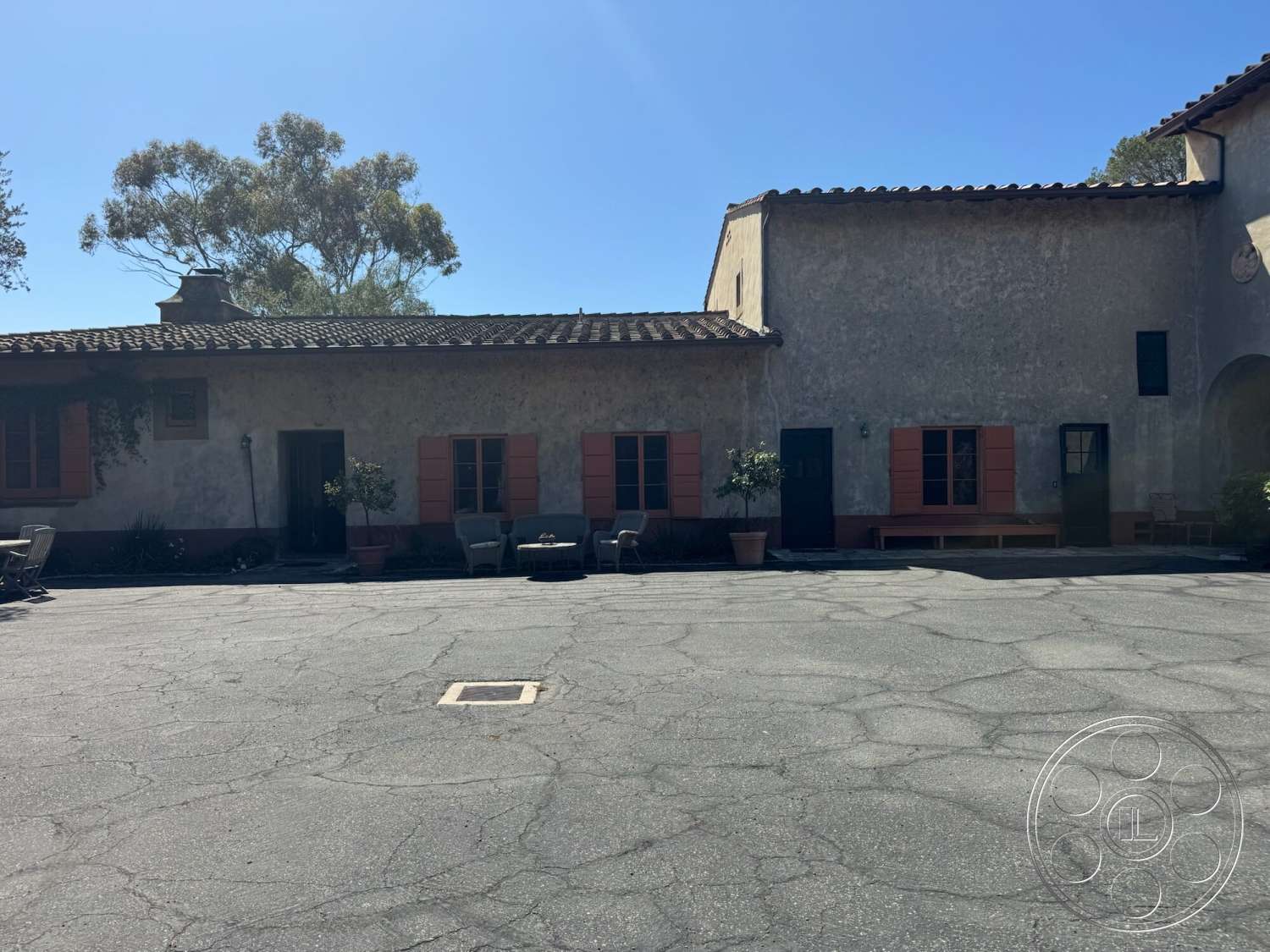 Farmstead Garden - exterior, stucco walls, arched entryway, terra cotta roof tiles, paved courtyard, ornamental landscaping, metal door frames, wood framed windows, clay planters, black painted doors, pink shutters, adjacent outdoor seating area, weathered exterior finishes
