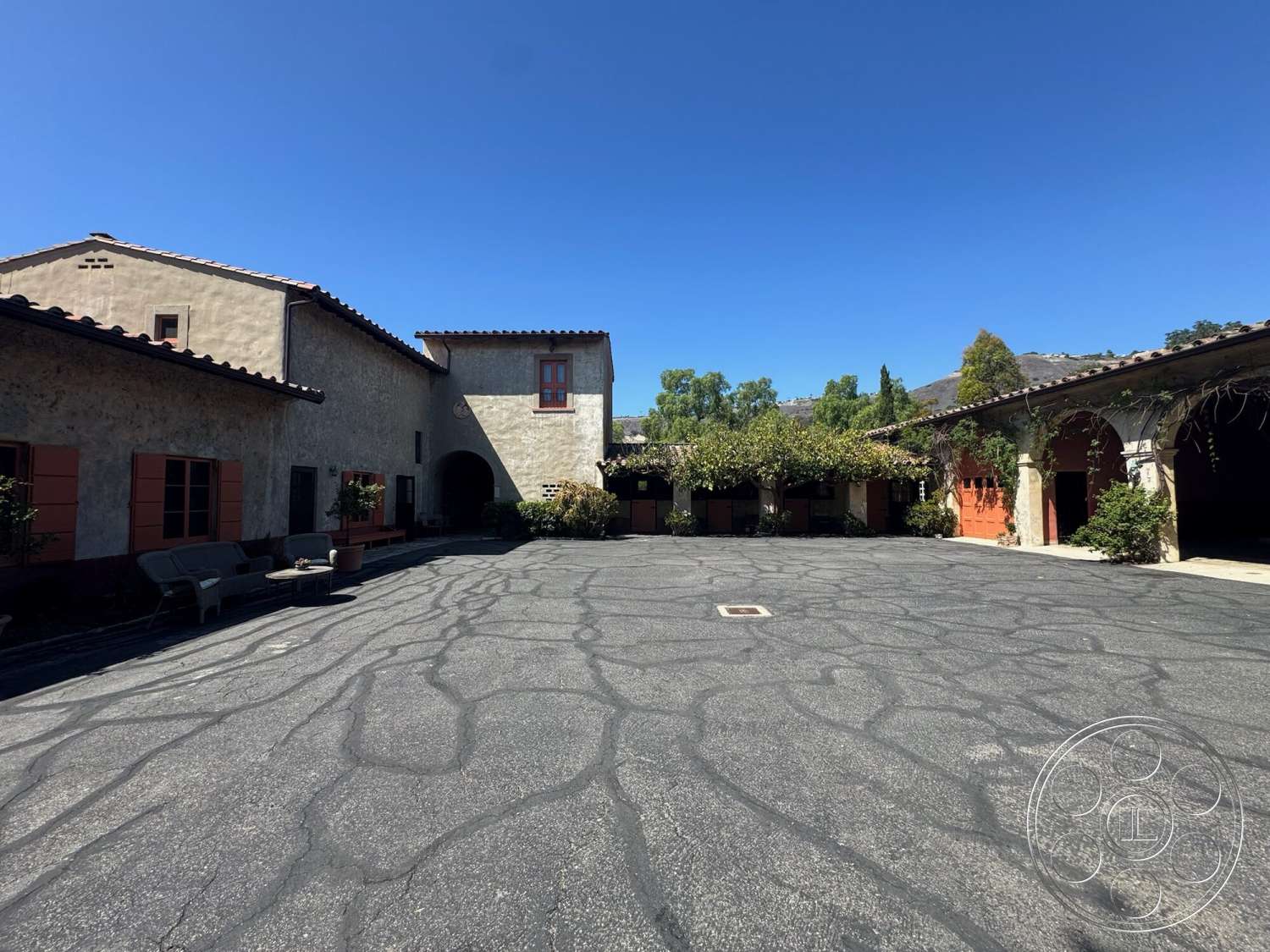 Farmstead Garden - exterior, outdoor seating area, circular driveway, asphalt driveway, arched entryway, tile roof, stone planters, red wooden window frames, mountain view setting, landscaped garden area, stucco exterior walls, decorative archways, vines on pergola