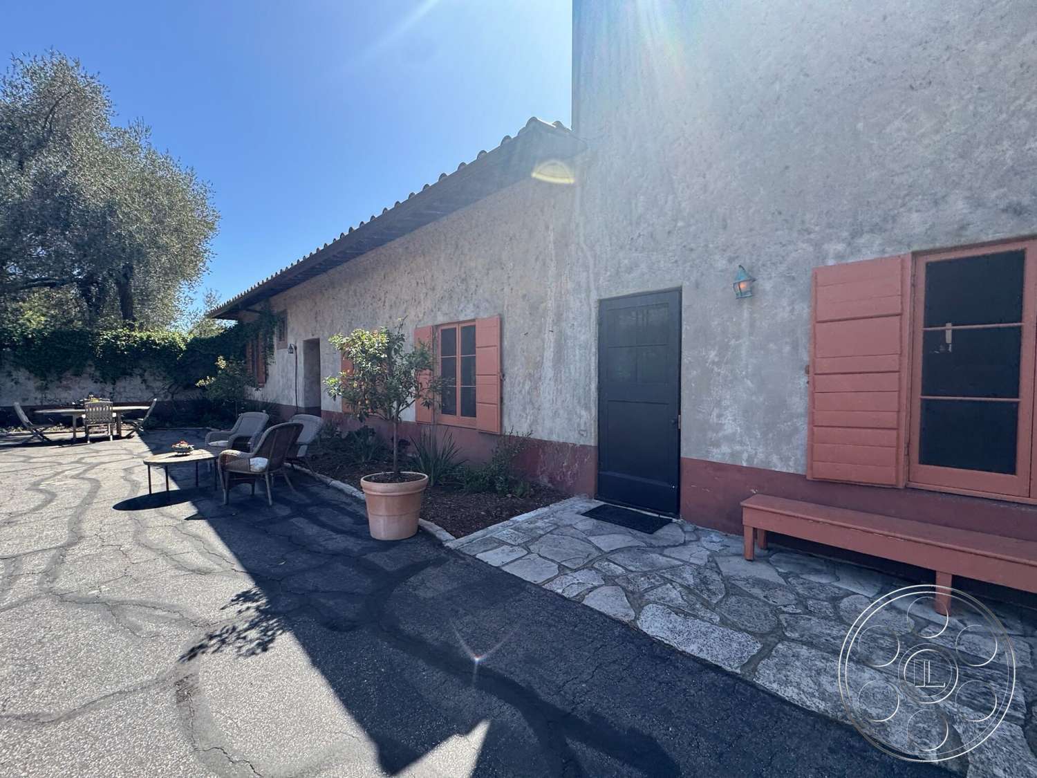 Farmstead Garden - exterior, concrete driveway, modern lighting fixture, country home, landscaped garden area, courtyard setting, flagstone patio flooring, open seating area, stucco building walls, red shuttered windows, simple wooden outdoor bench, rustic style architecture