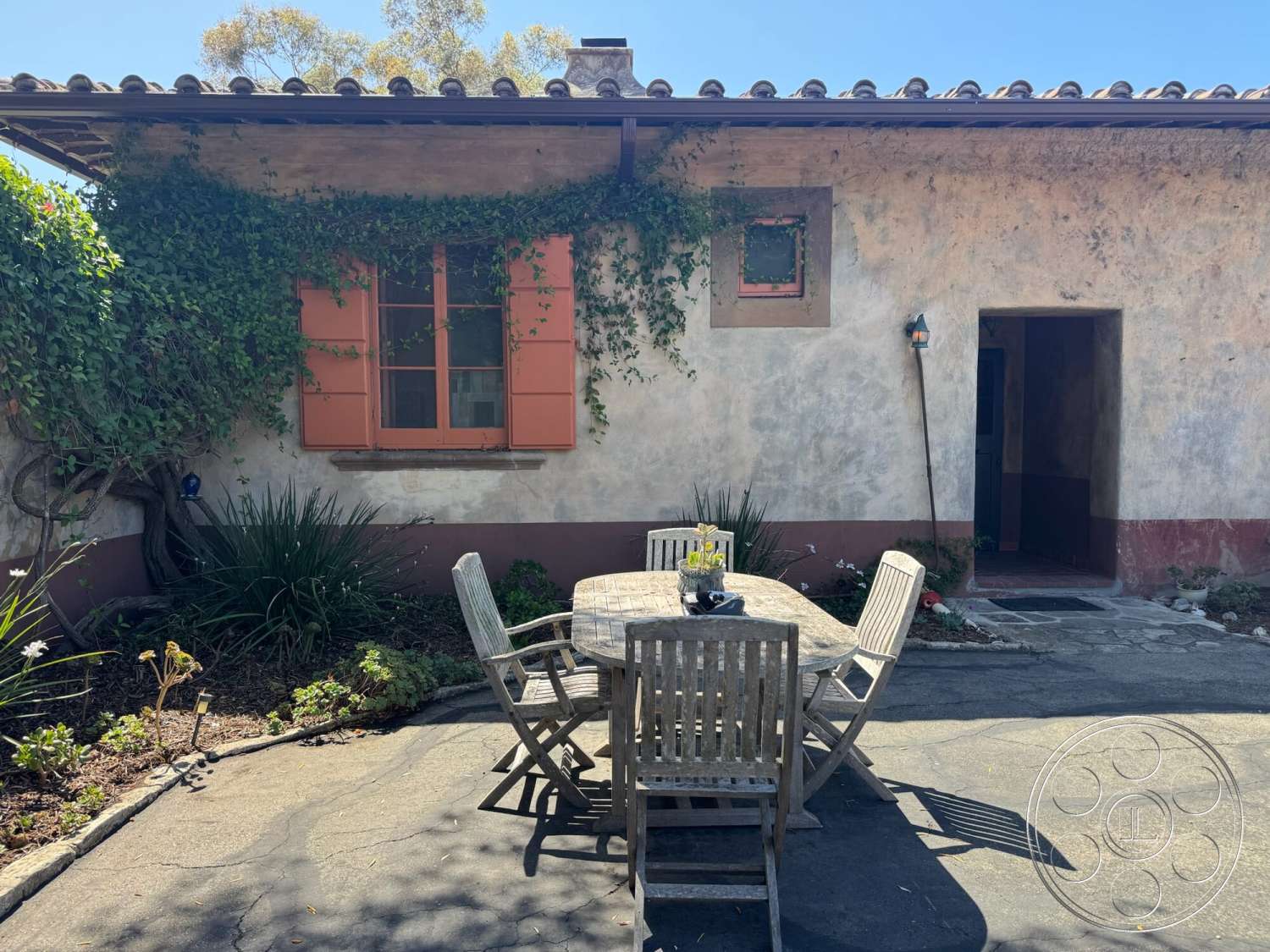 Farmstead Garden - exterior, wooden dining table, outdoor dining area, decorative lantern, wooden dining chairs, wooden window shutters, landscaped garden beds, stucco wall exterior, flagstone patio flooring, red-tiled roof, vine-covered wall, vivid greenery