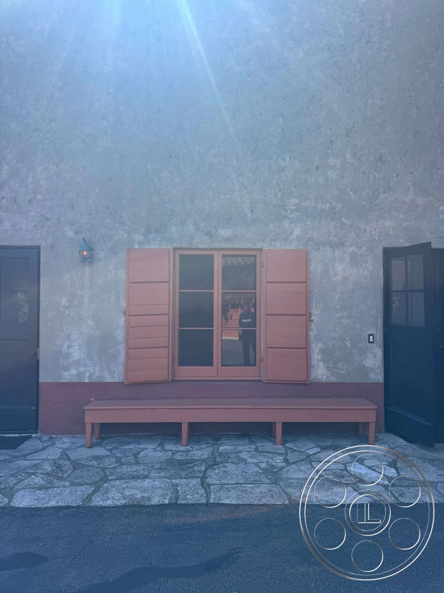 Farmstead Garden - exterior, wooden bench seating, decorative wall sconce, dark wood door, gray stone facade, wooden window shutters, stucco wall finish, stone patio flooring, glass window panels, earth-toned wall base