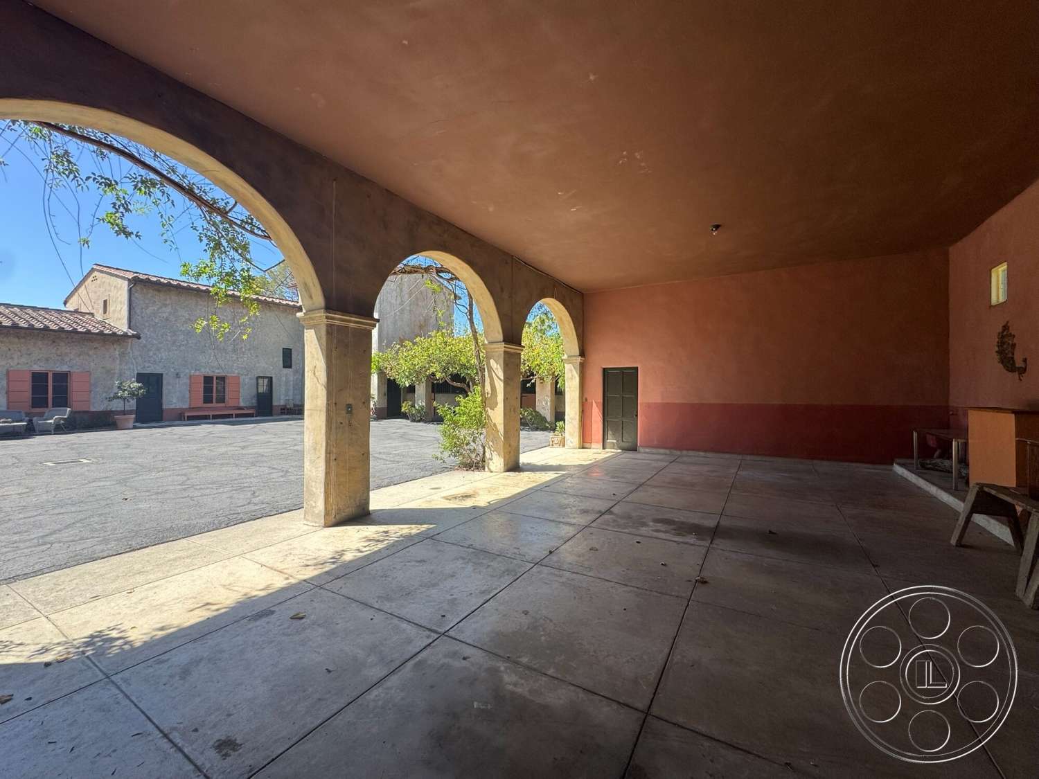 Farmstead Garden - exterior, outdoor seating area, gravel pathway, textured plaster ceiling, stucco walls, arched doorways, terracotta tile roof, ambient natural light, paved courtyard, greenery accent, rustic architectural style, reinforced concrete floor