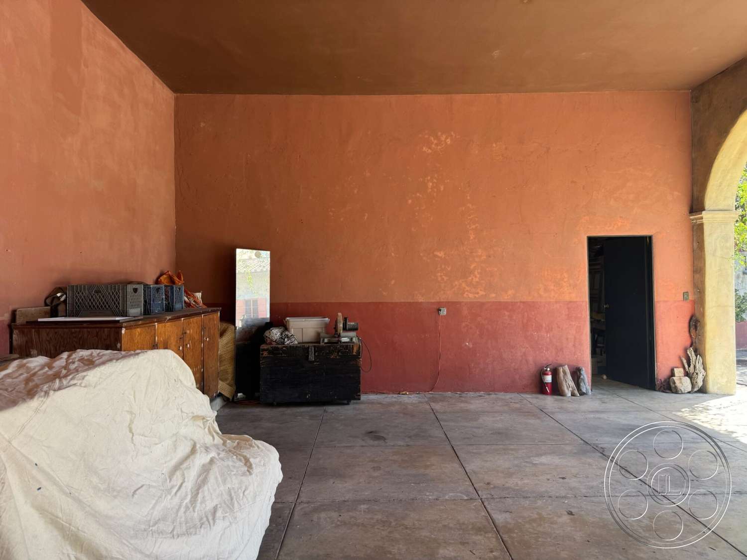 Farmstead Garden - light fixture, exposed ceiling, textured plaster walls, open doorway, mirror reflection, wood cabinet storage, rust-colored wall paint, bare concrete floor, dark wooden storage box