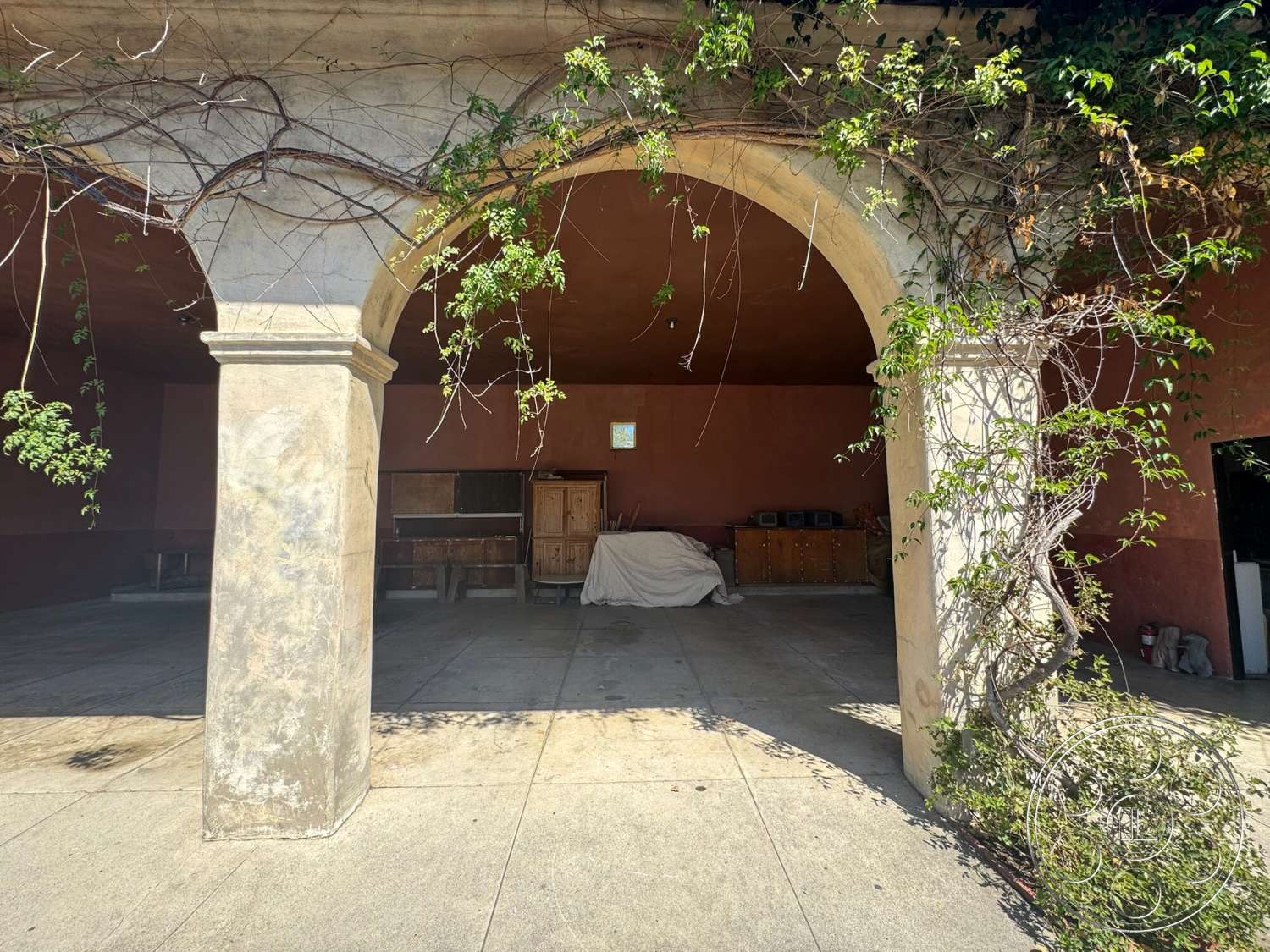 Farmstead Garden - natural light, exterior, concrete floor, wooden furniture, landscaped surroundings, open outdoor space, stone columns, stucco wall finish, arched stone entrance, terracotta wall color, vines on arches
