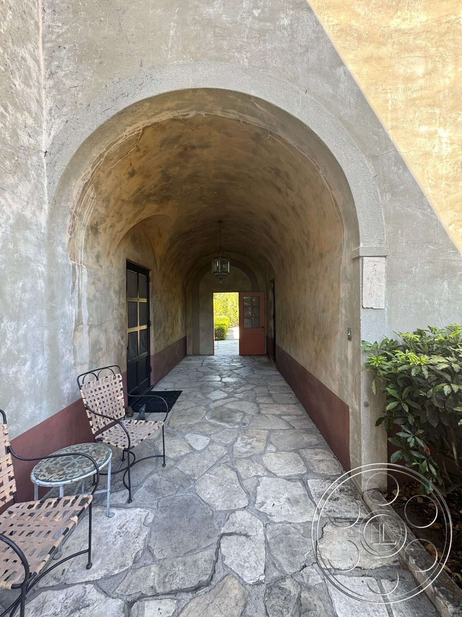 Farmstead Garden - exposed concrete wall, metal table, arched entryway, courtyard entrance, iron patio chairs, textured plaster wall, rustic outdoor setting, flagstone walkway flooring, landscaped exterior garden