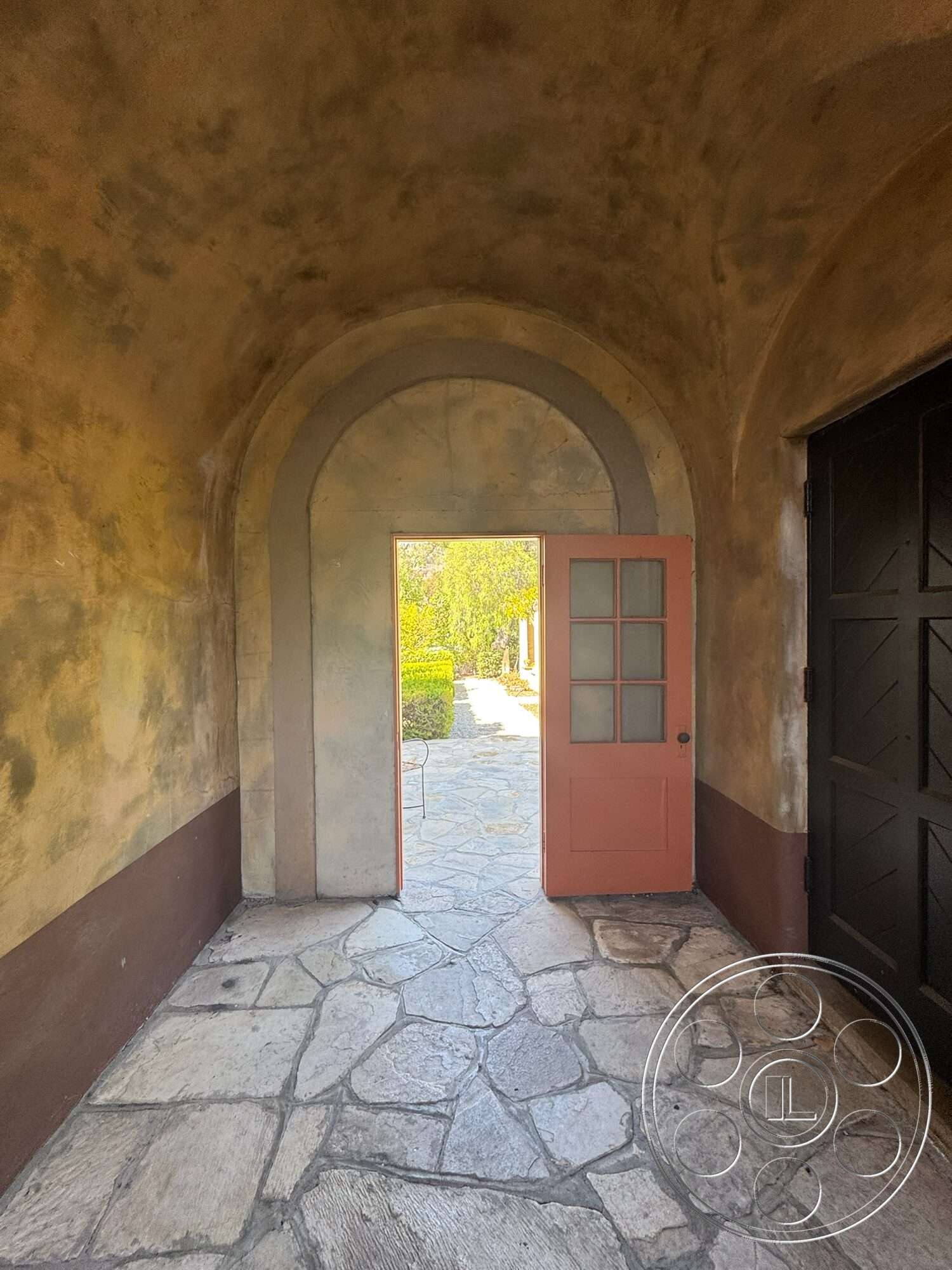 Farmstead Garden - exterior, garden view, stone flooring, vaulted ceiling, textured plaster walls, arched entryway, landscaped path, double door entry, brown painted wall, pink wooden door