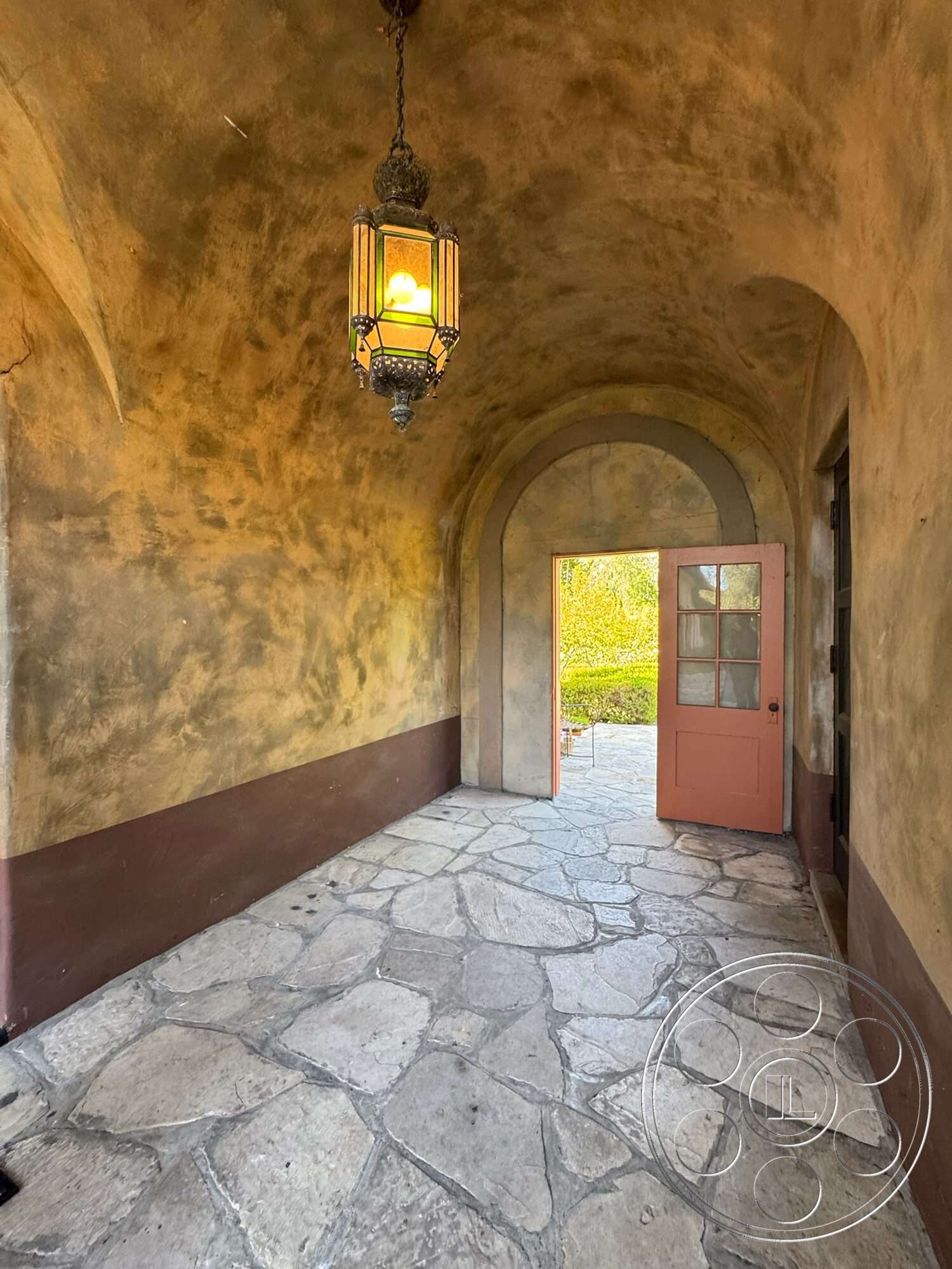 Farmstead Garden - wooden door, arched doorway, decorative pendant lighting, textured plaster wall, plastered wall finish, exposed stone flooring, earth-tone wall colors