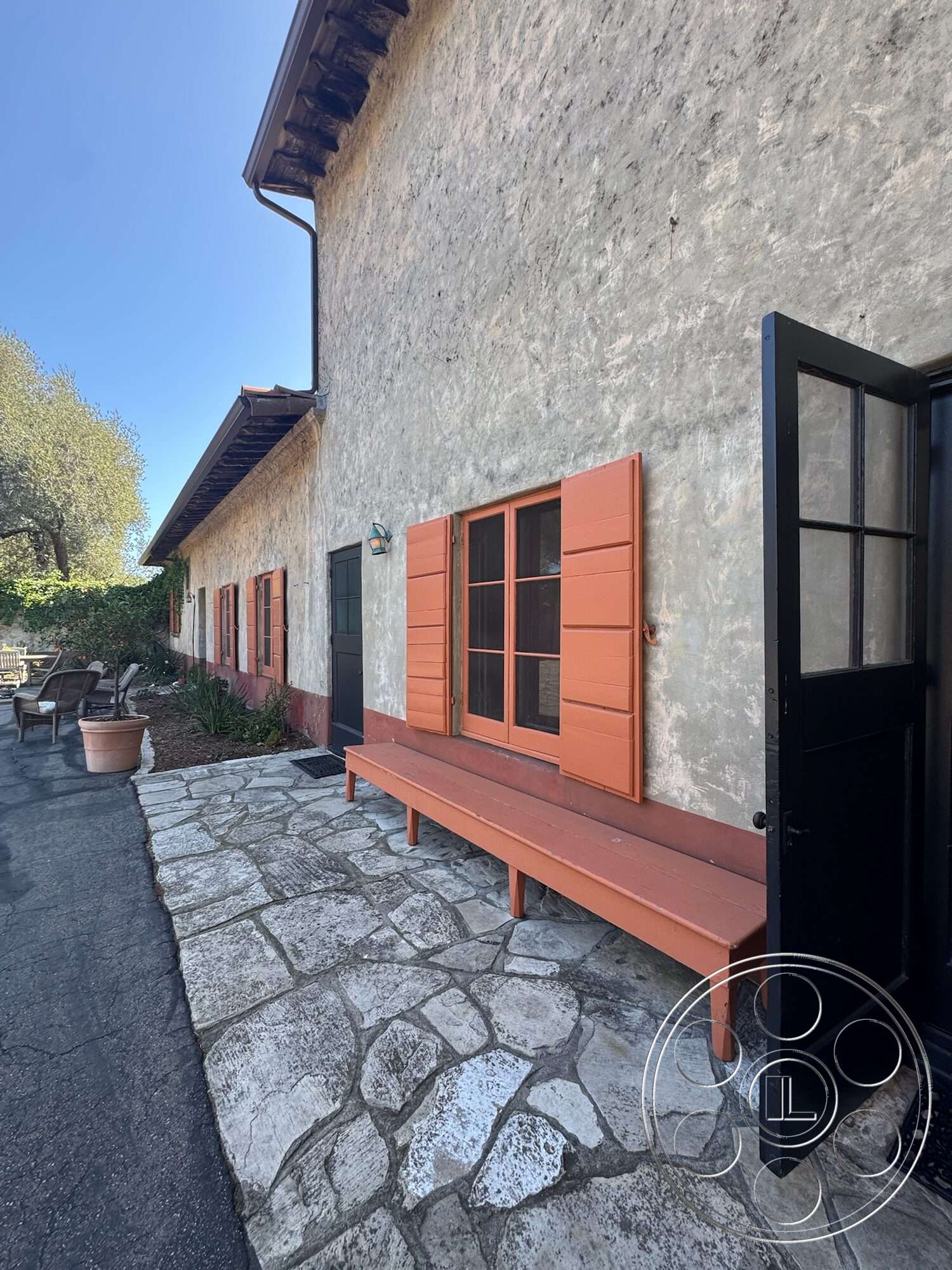 Farmstead Garden - exterior, landscaped garden, wooden bench, slate stone pathway, cobblestone patio, stucco walls, black metal door, terracotta painted window shutters, exposed wooden eaves
