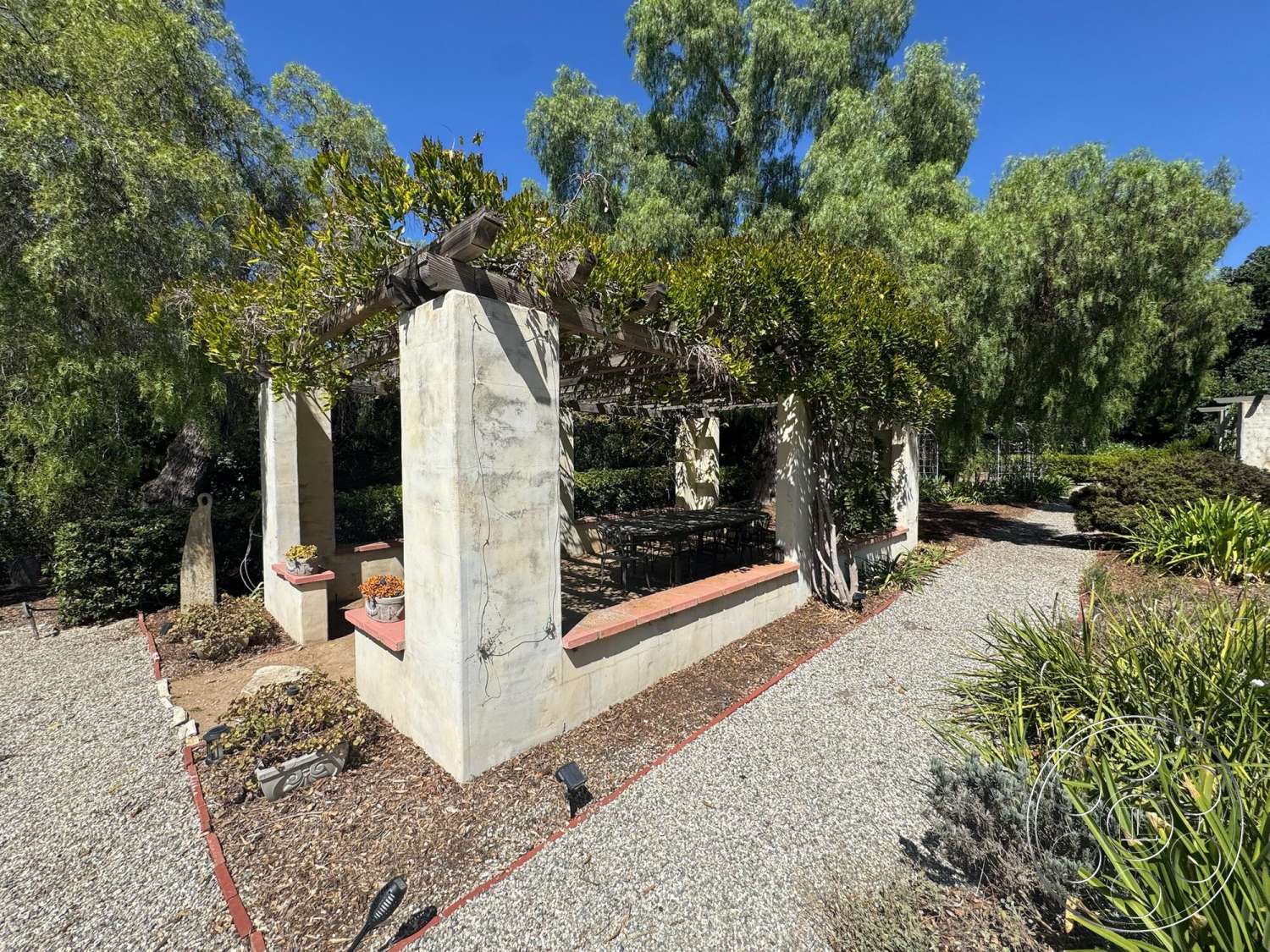 Farmstead Garden - exterior, potted plants, gravel pathway, textured plaster walls, landscaped garden setting, steel outdoor furniture, red brick border, plaster pergola columns, wooden trellis beams, bordering shrubs, natural sunlight filtering through leaves