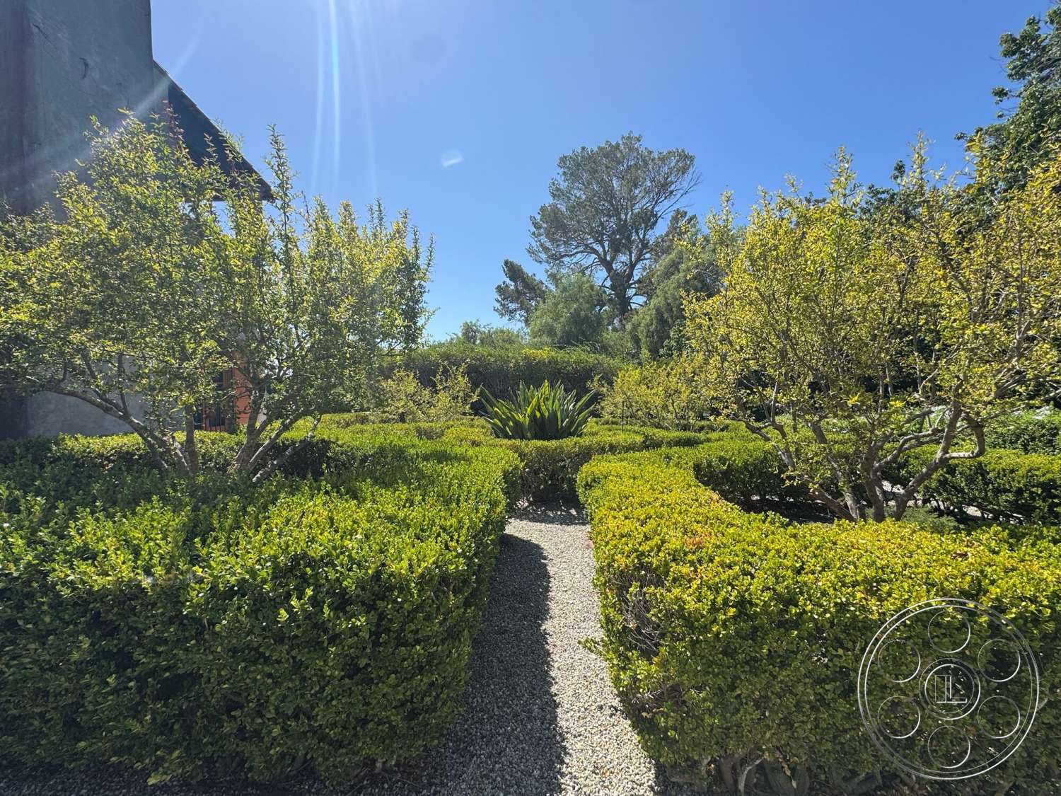 Farmstead Garden - exterior, gravel pathway, blue sky, natural sunlight, landscaped garden area, lush green foliage, boxwood hedge landscaping, visible trees