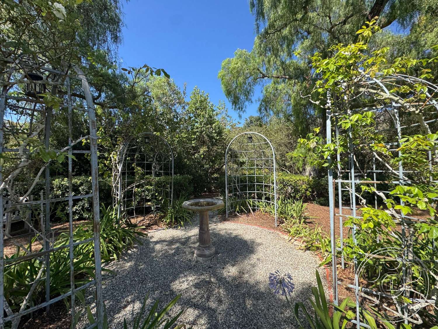 Farmstead Garden - exterior, lush greenery, natural landscaping, flowering plants, dappled sunlight, circular garden layout, gravel garden pathway, sunny garden setting, metal garden trellises, birdbath fountain
