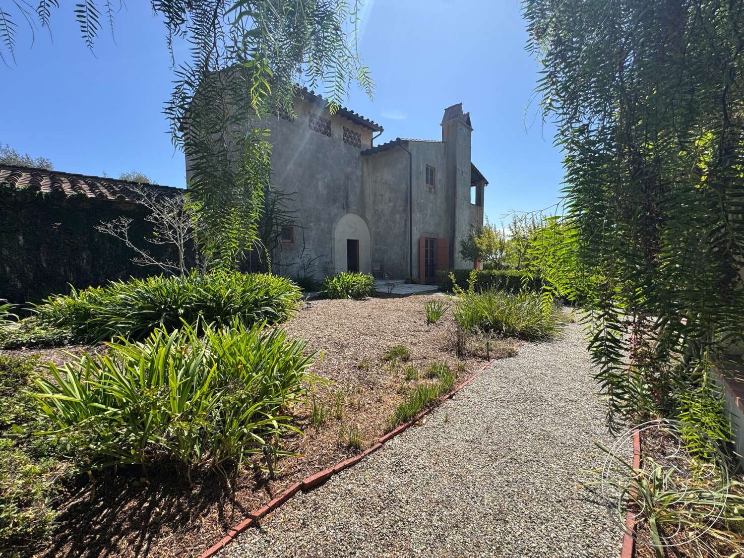 Farmstead Garden - exterior, landscaped garden, gravel pathway, terracotta roof tiles, stucco walls, arched doorway, tall windows, native vegetation, central courtyard, rustic architectural style