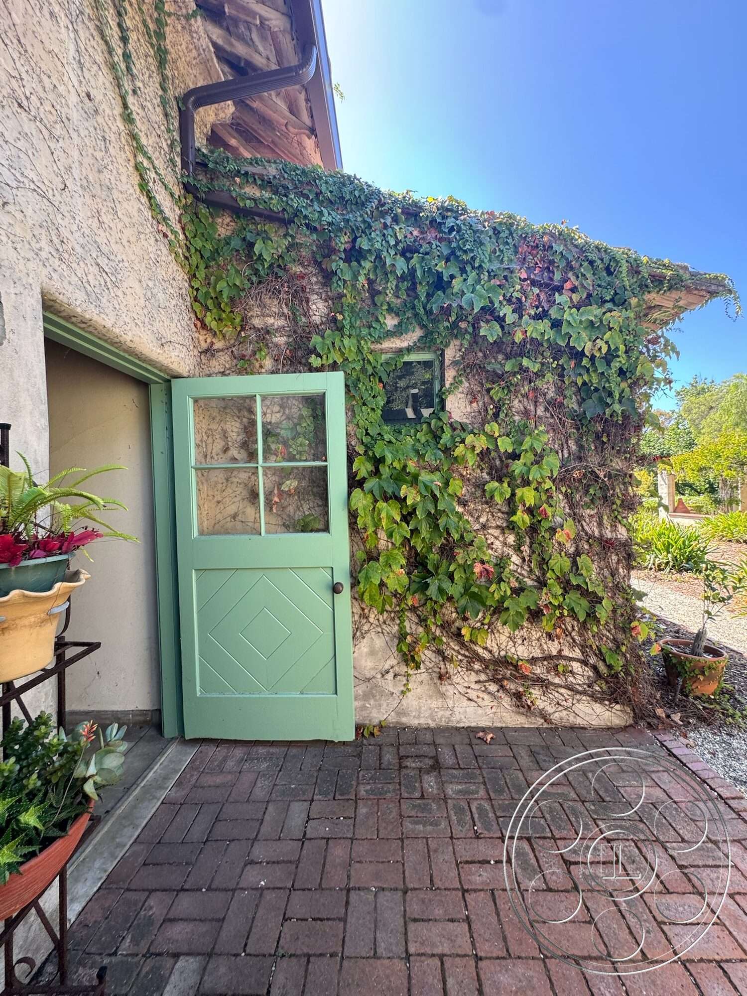 Farmstead Garden - exterior, brick pathway, flower pots, stucco wall, landscaped garden area, textured plaster wall, vine-covered wall, green wooden door, natural green foliage