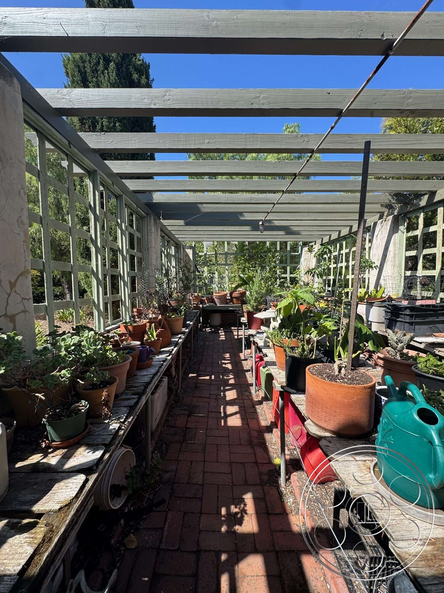 Farmstead Garden - exterior, green foliage, outdoor workspace, gardening tools, horizontal wood slats, wood pergola structure, sunlit garden area, brick patio flooring, terracotta plant pots, wood plant benches