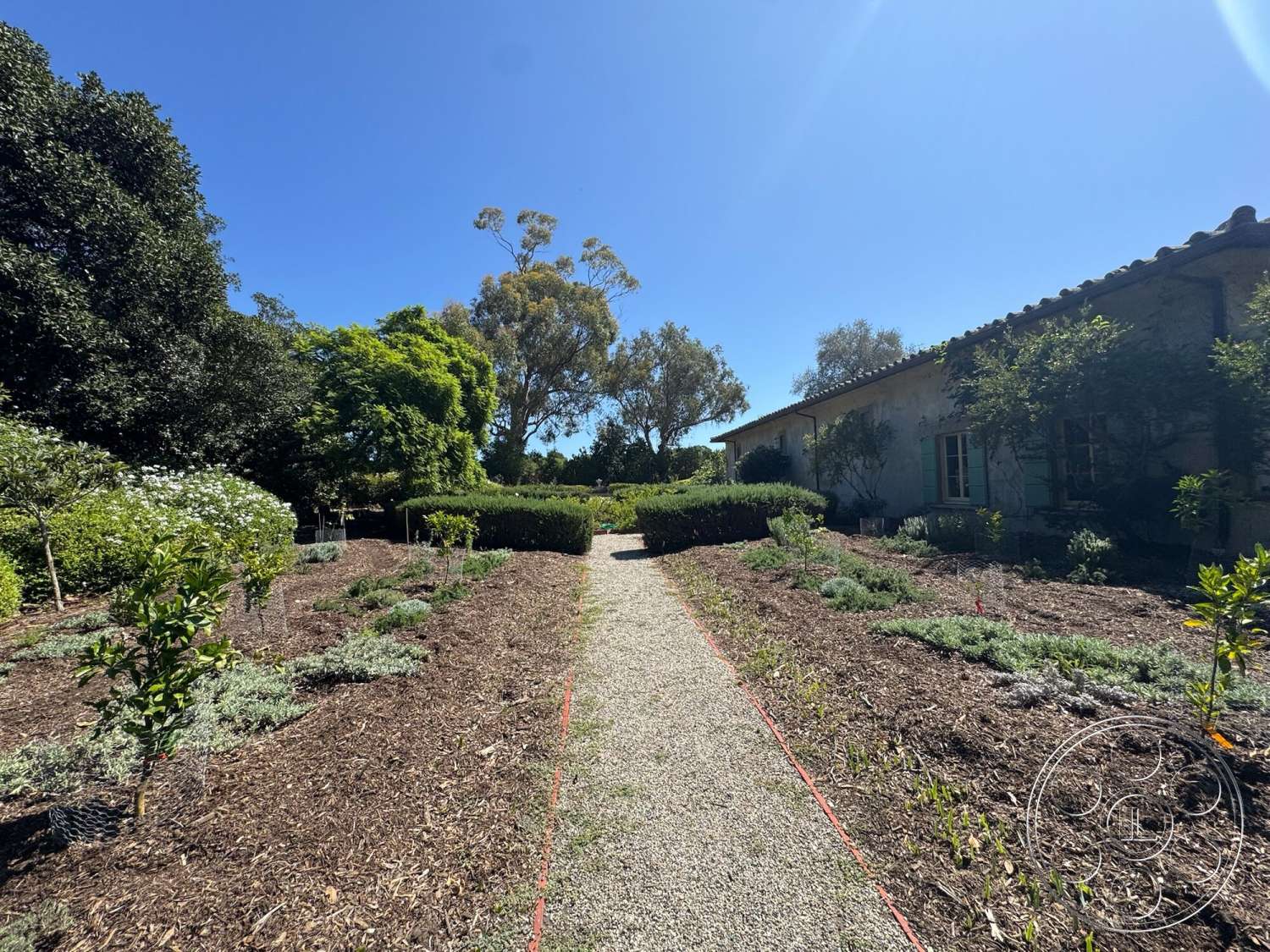 Farmstead Garden - landscaped garden, native plants, gravel pathway, flowering shrubs, outdoor garden, tile roof, hedge borders, wooden window shutters, sunny outdoor setting, exterior stucco walls, rural property, mulch garden beds