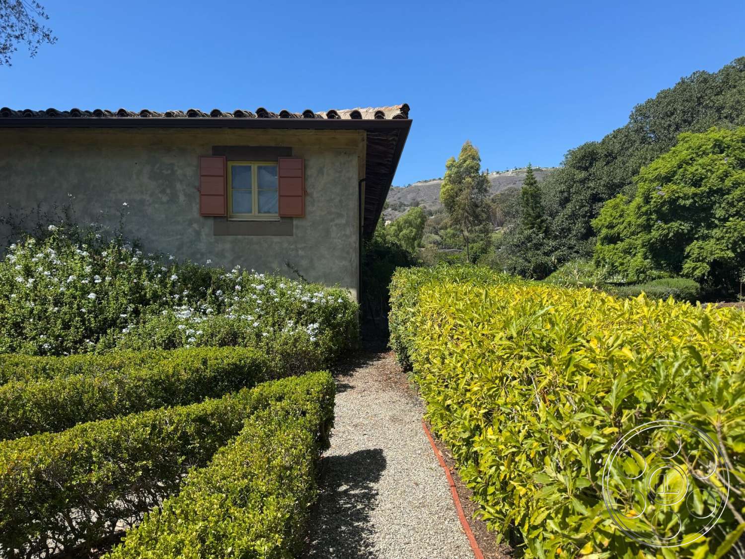 Farmstead Garden - exterior, landscaped garden, flowering shrubs, mountain view, stucco walls, boxwood hedges, cobblestone pathway, sunny outdoor setting, wood window shutters, sloped tile roof